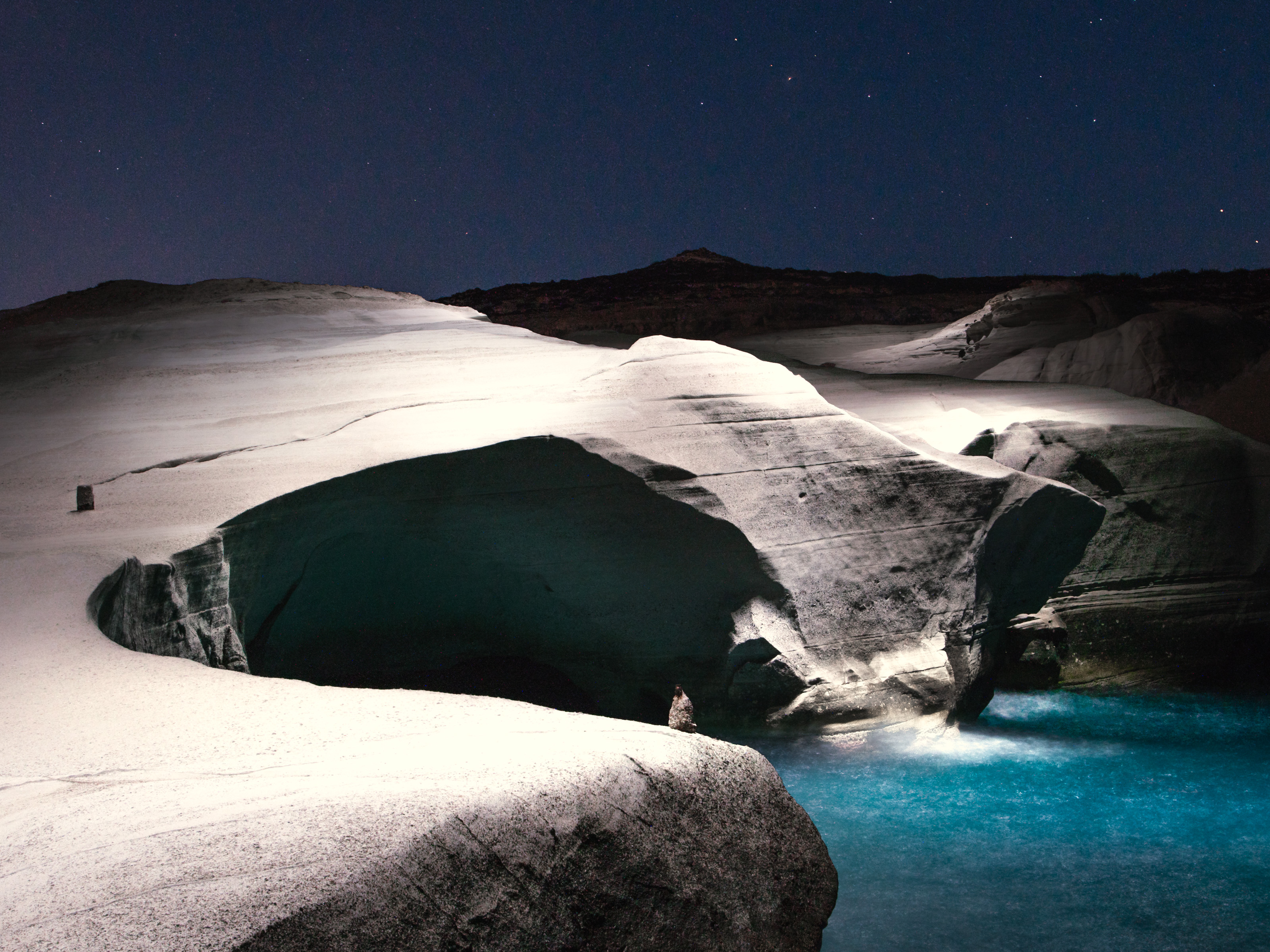 White rock formations beside bright blue water under a starry night sky, softly illuminated—perfect inspiration for a fine artist seeking otherworldly beauty.