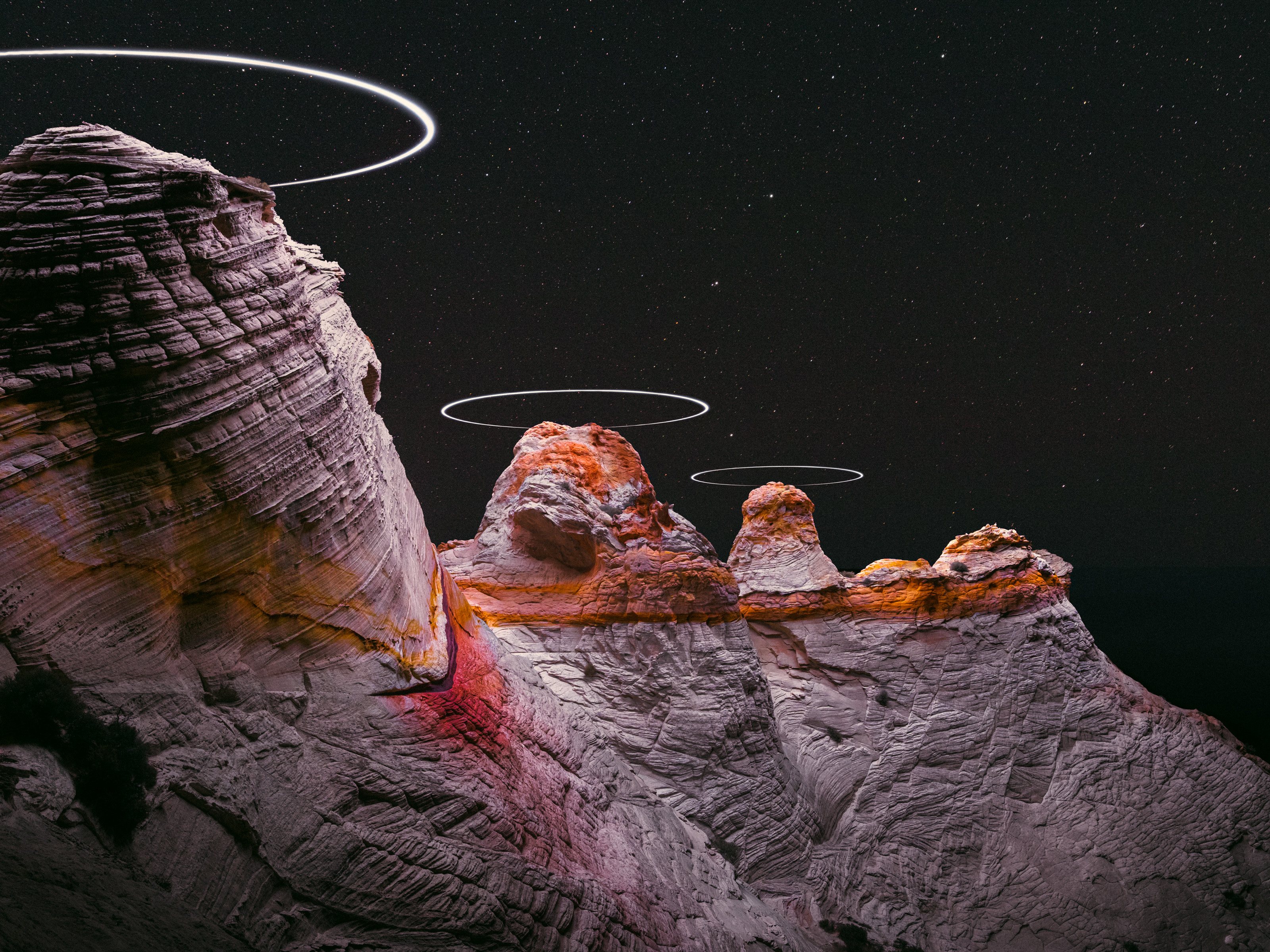 Night sky over rocky cliffs with glowing, futuristic rings above the peaks, resembling drone light painting or UFO light trails.