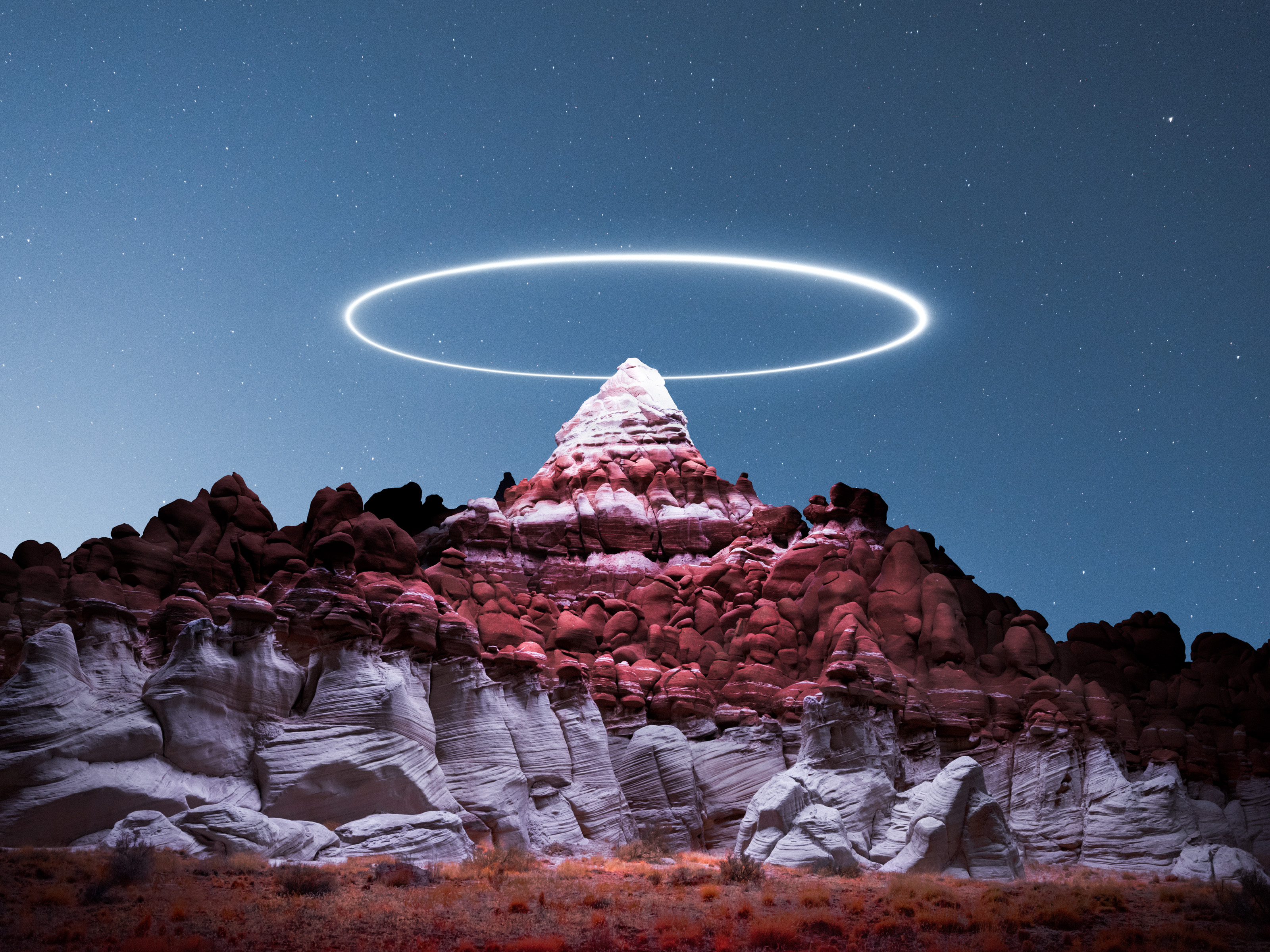 A glowing white ring hovers above a rocky mountain peak under a starry night sky, creating a mesmerizing scene of drone light painting in this nighttime landscape photography.