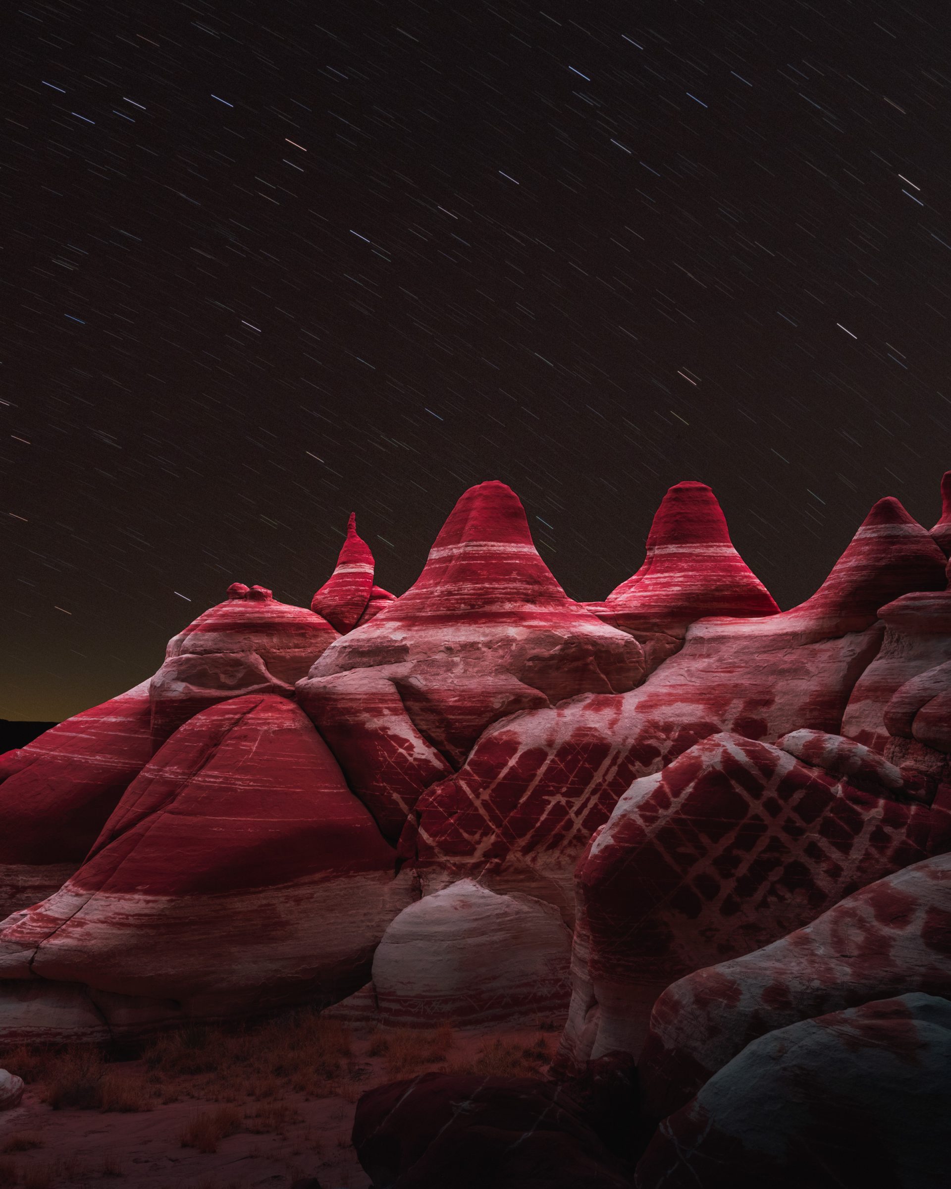 Red and white striped rock formations under a night sky with visible star trails above, capturing the magic of nighttime landscape photography.
