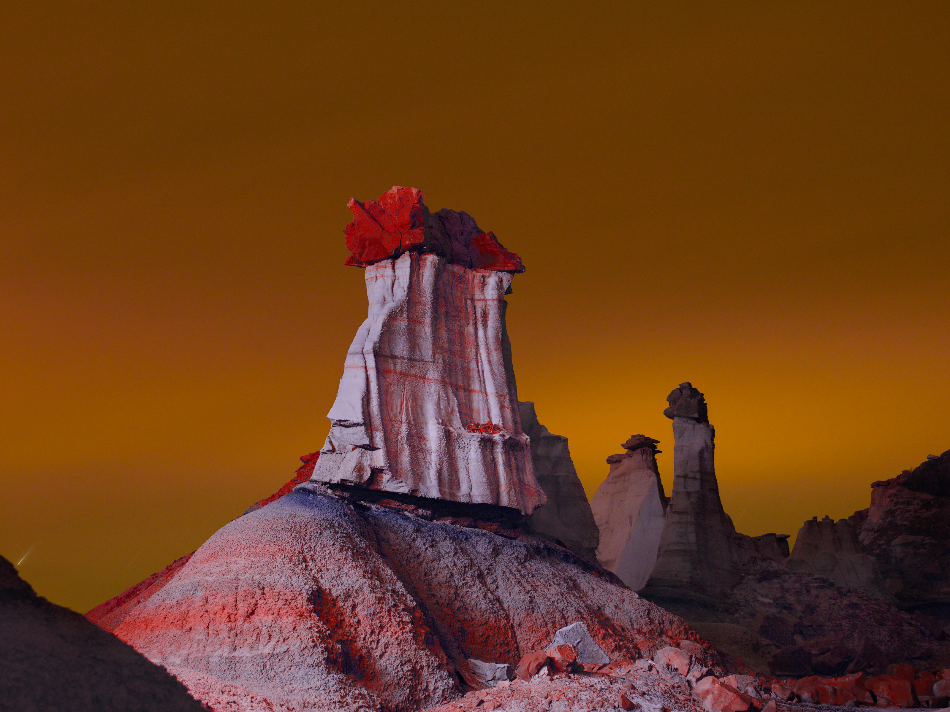 A tall, striped rock formation with a red top stands under an orange-yellow sky at dusk, inviting any photographer passionate about nighttime landscape photography to capture its unique beauty.