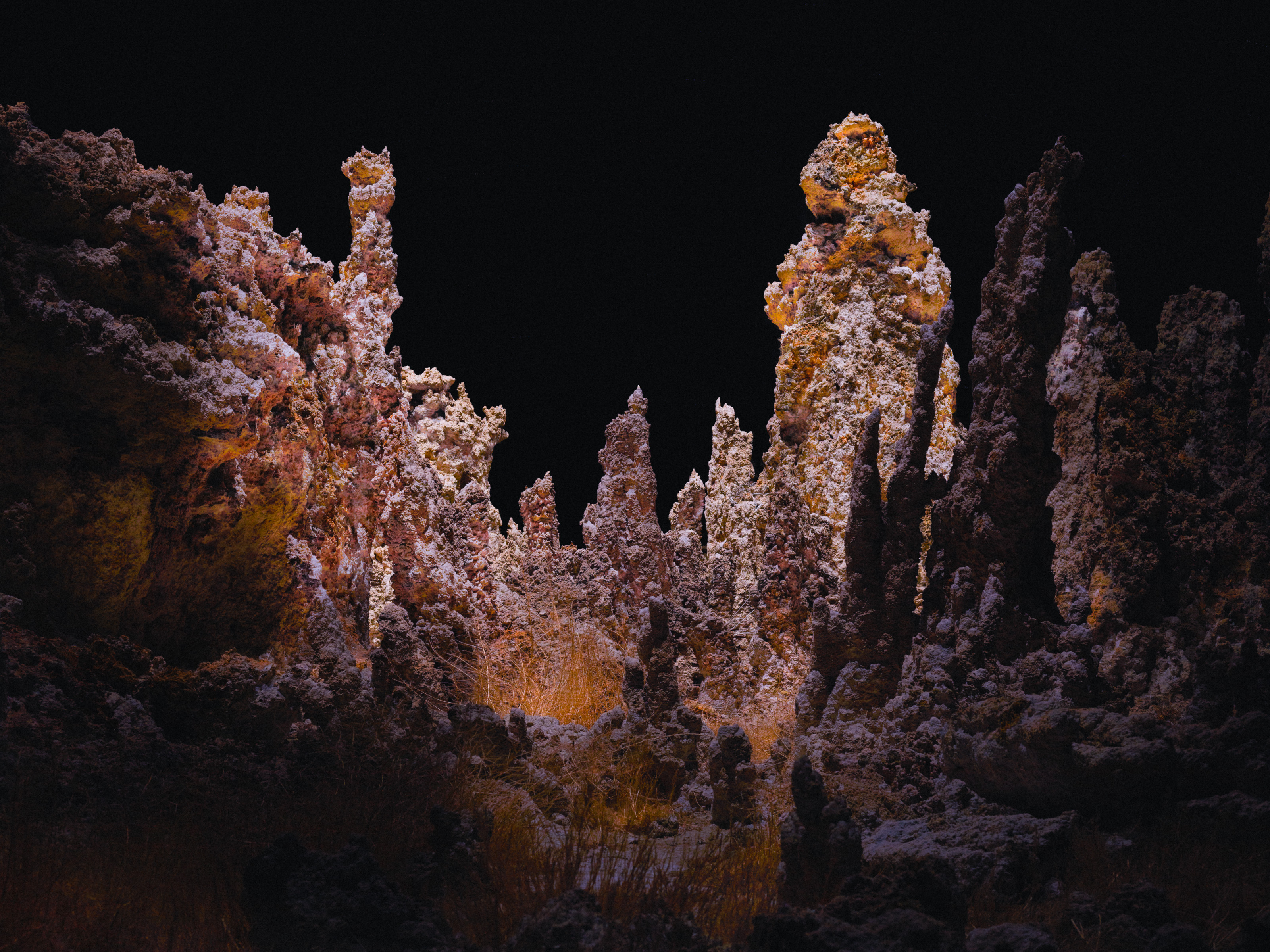 Rocky spires and formations stand tall under dramatic lighting against a dark night sky, creating a stunning scene for nighttime landscape photography.