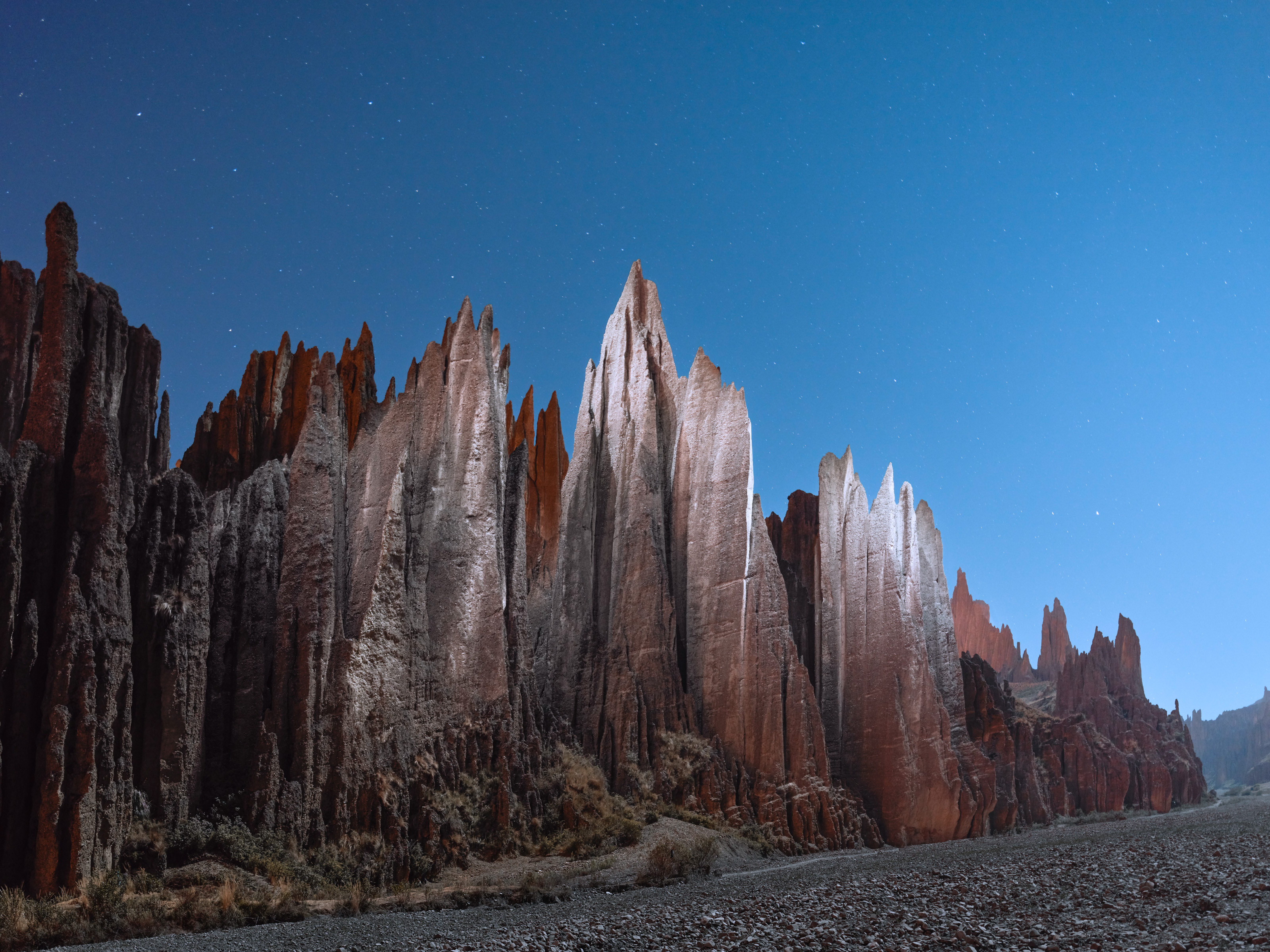 Jagged red rock formations rise under a clear, starry night sky in a rugged, desert-like landscape, evoking the dramatic vision of a fine artist’s nighttime landscape photography.