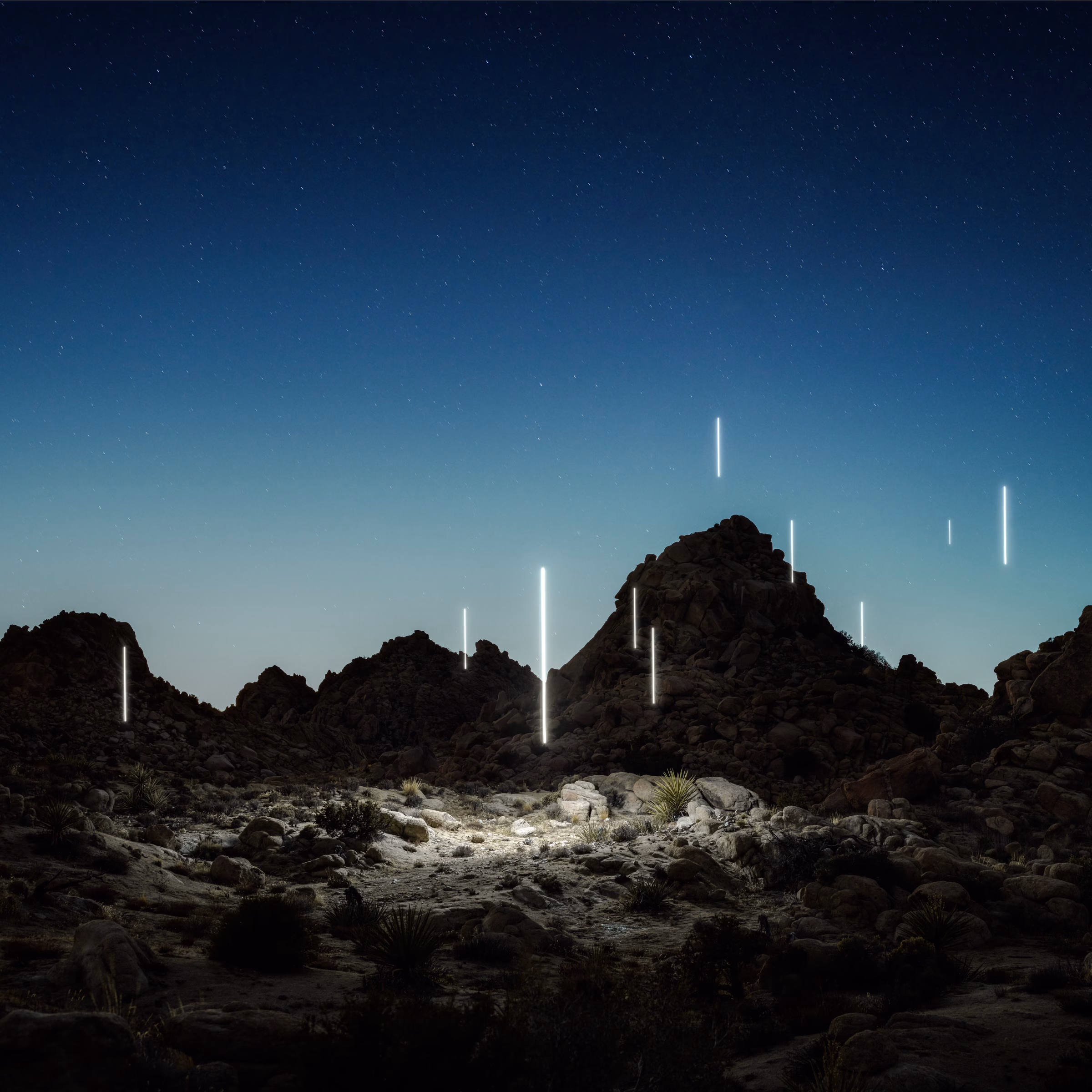 Rocky desert landscape at dusk with glowing vertical light beams scattered among the hills under a starry sky, evoking the magical atmosphere of Live From Joshua Tree by Rüfüs Du Sol.