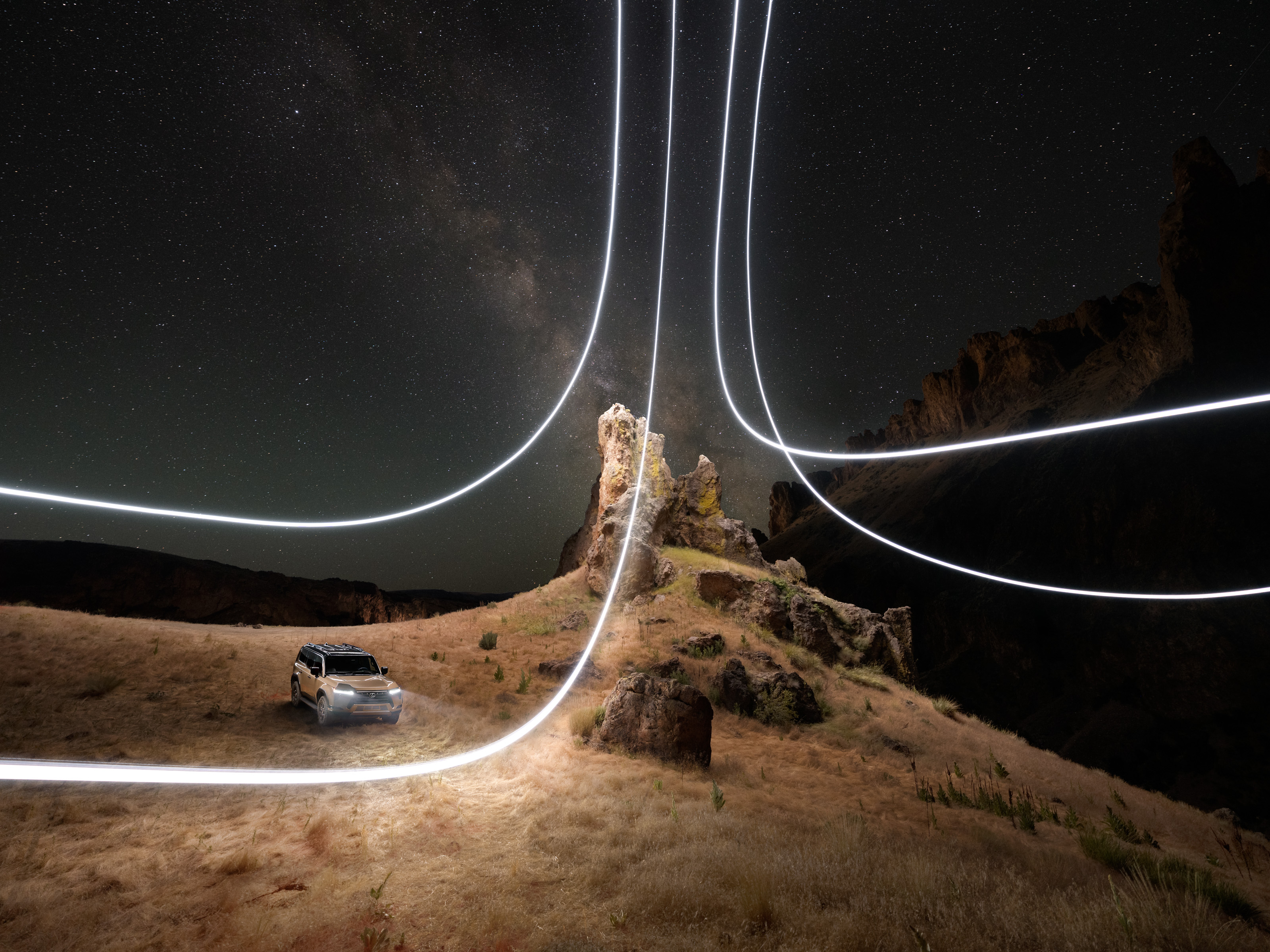 A car on dry grass at night with glowing light trails and a starry sky in the background, captured by a photographer skilled in nighttime landscape photography.