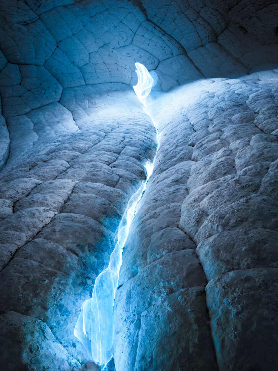 Blue light glows in a crack on a rough, textured rock surface, creating an ethereal and mysterious effect reminiscent of fine artist-inspired drone light art.