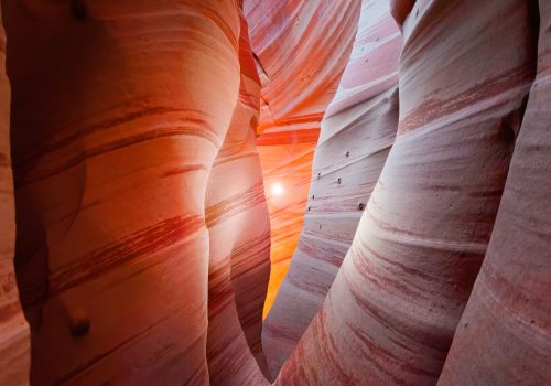 Narrow slot canyon with red striped walls and sunlight shining through an opening, captured by a photographer as drone light painting illuminates the natural curves.