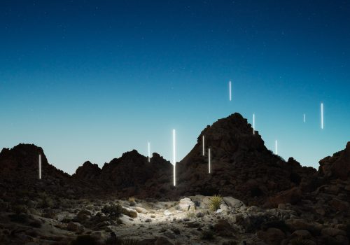Desert landscape at twilight with glowing vertical light beams scattered among rocky hills, showcasing the magic of nighttime landscape photography.