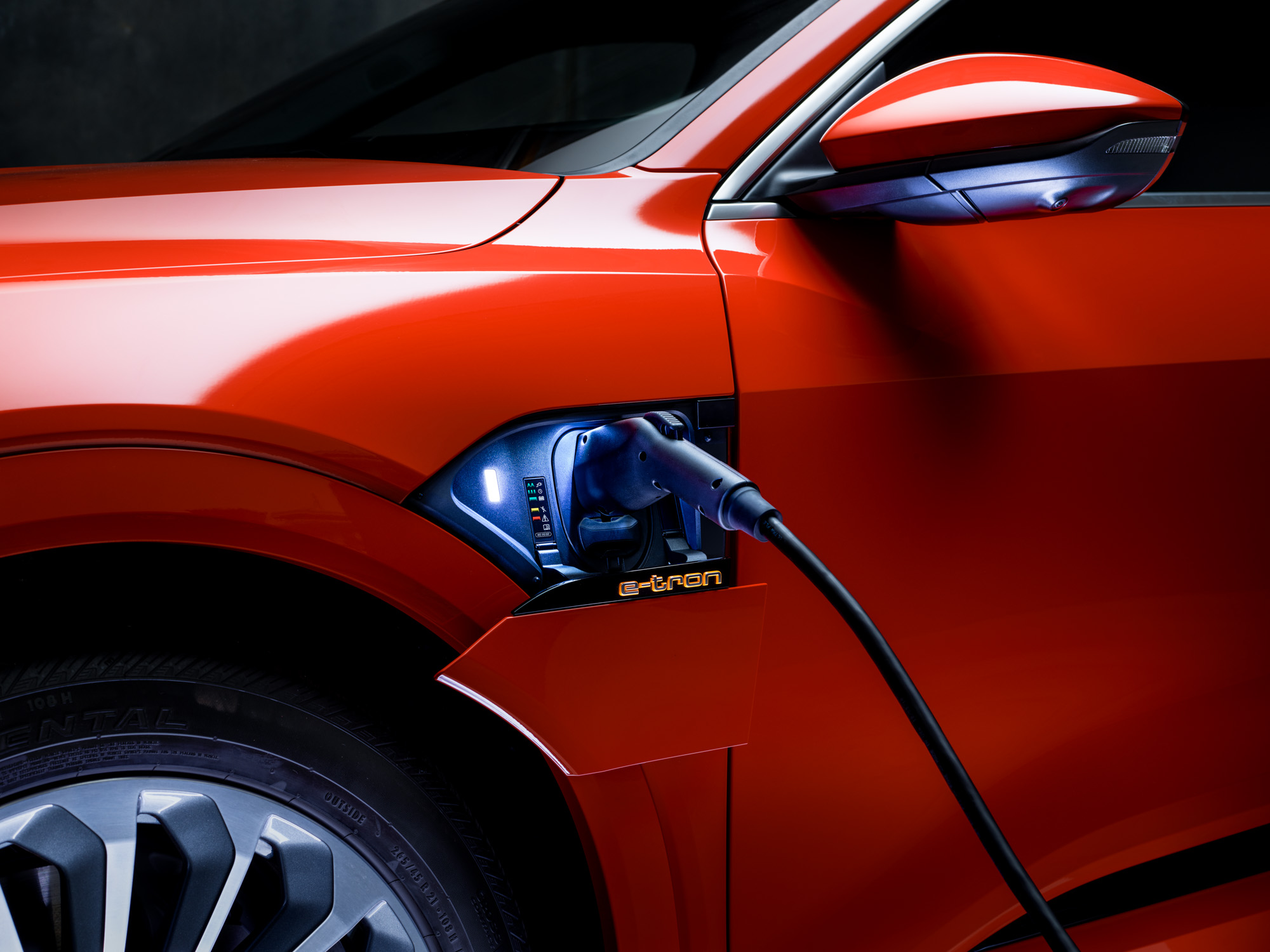 Close-up of an orange electric car charging, with the cable plugged in near the front wheel—captured by a talented photographer who highlights modern mobility through striking visuals.