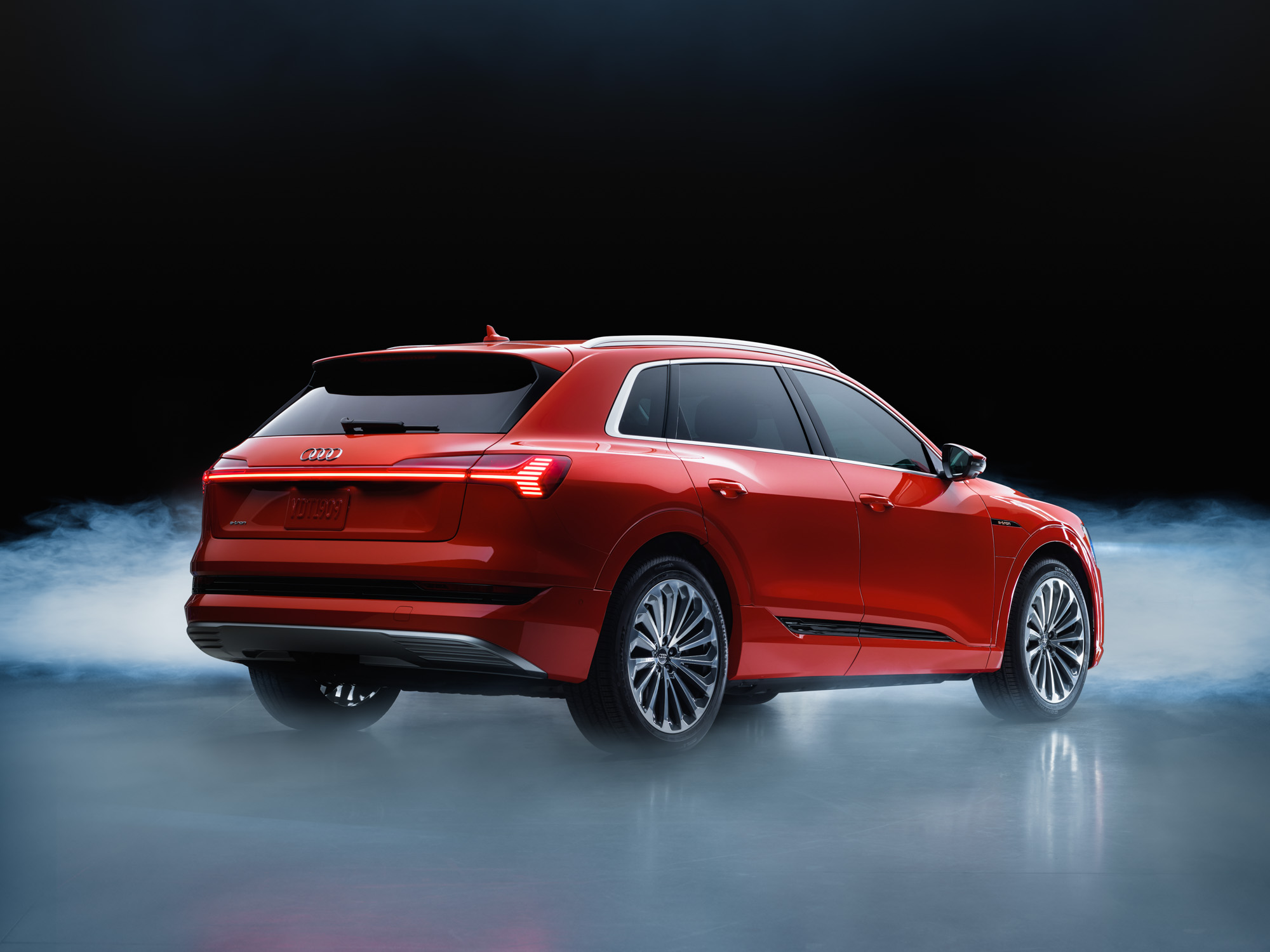 Red Audi SUV parked on a shiny surface with mist and a dark background, viewed from the rear side angle, reminiscent of nighttime landscape photography or a fine artist’s dramatic vision.