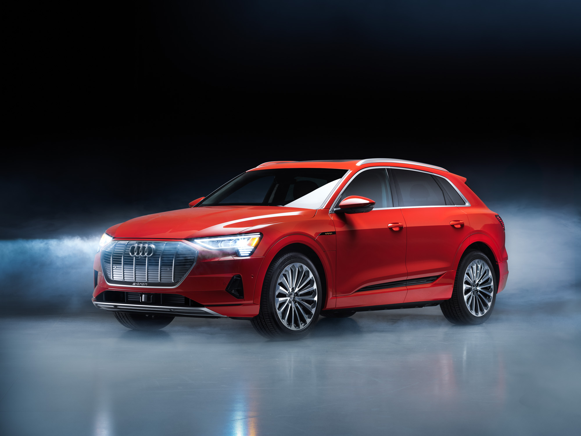 A red Audi e-tron SUV is parked on a glossy surface with mist and a dark, dramatic background, creating a futuristic scene worthy of a photographer’s nighttime landscape photography portfolio.