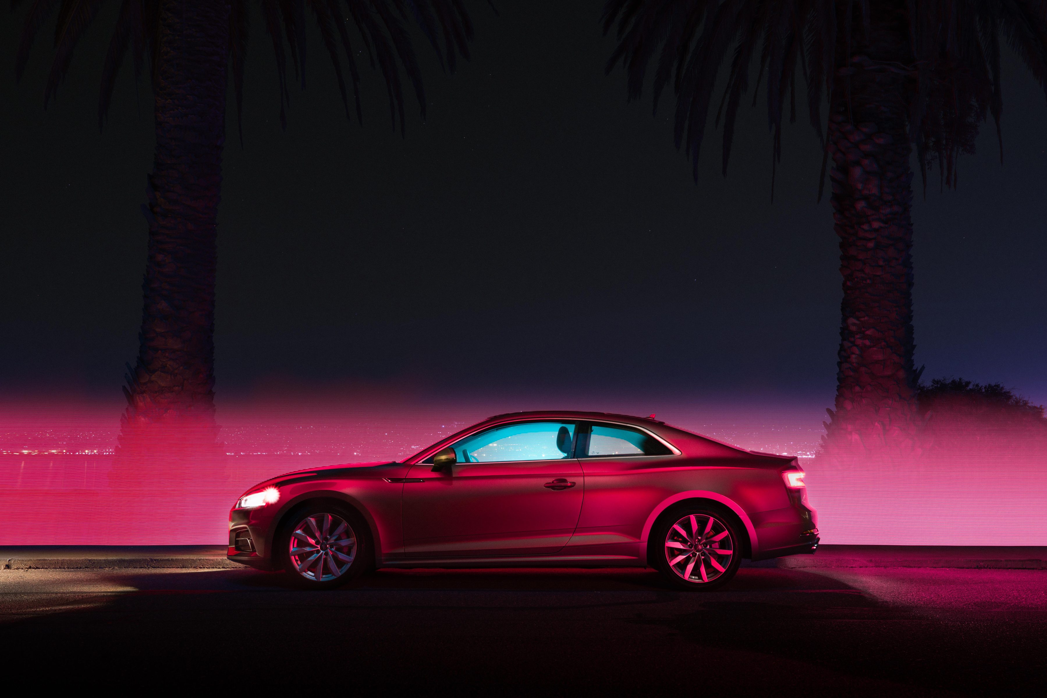 A red coupe parked at night between palm trees, illuminated by vibrant pink and blue lighting, captures the eye like a fine artist’s masterpiece or a photographer’s vivid dream.