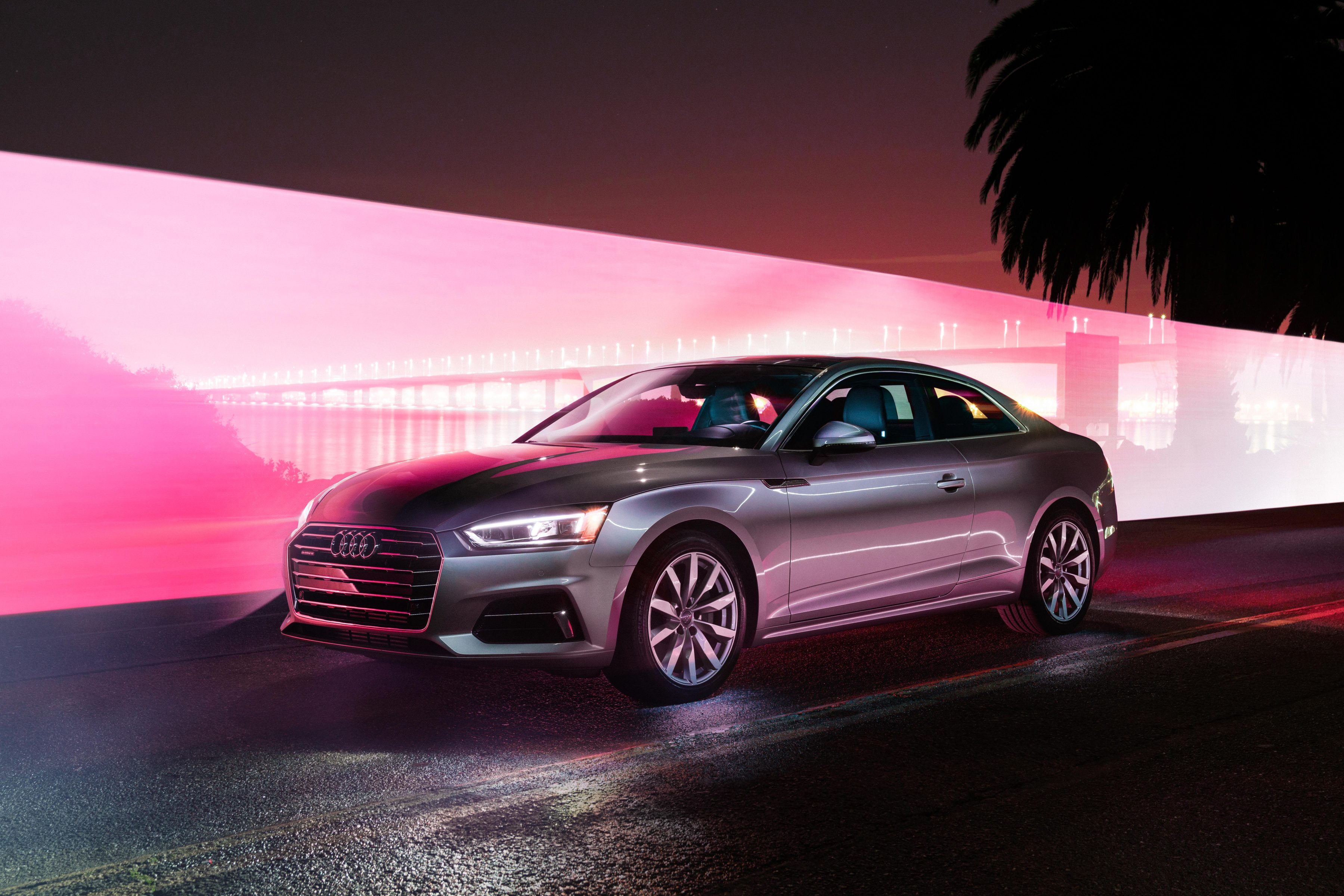 A silver Audi coupe parked at night with pink and white light trails in the background, capturing the essence of nighttime landscape photography.