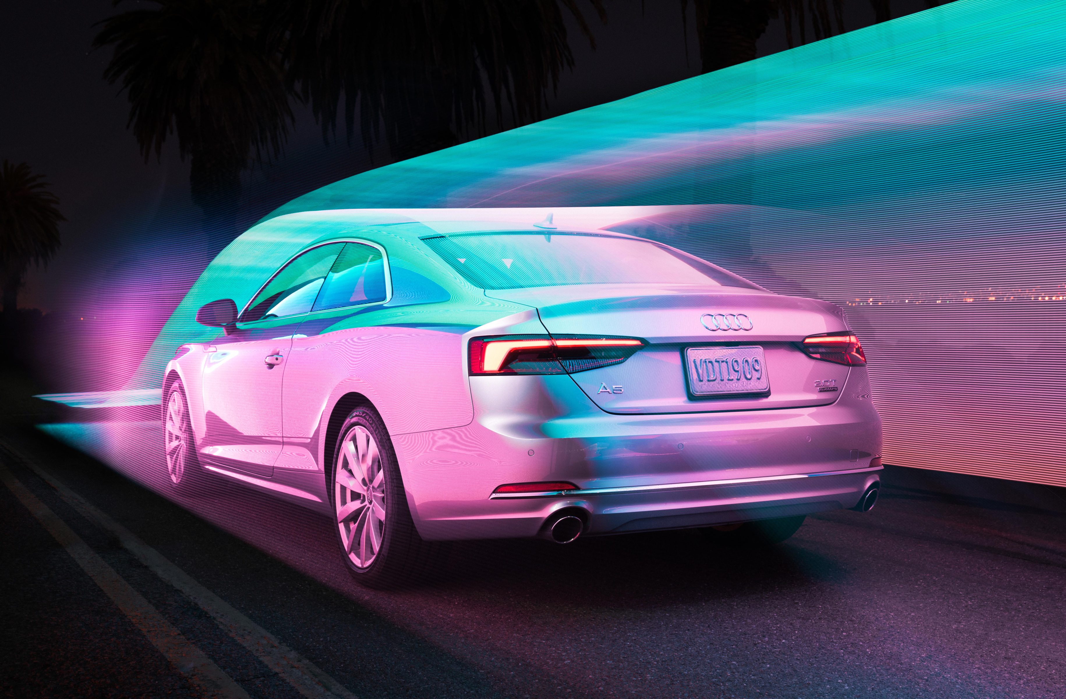 A silver Audi car drives at night with colorful neon light trails surrounding it, creating a futuristic scene reminiscent of drone light painting.