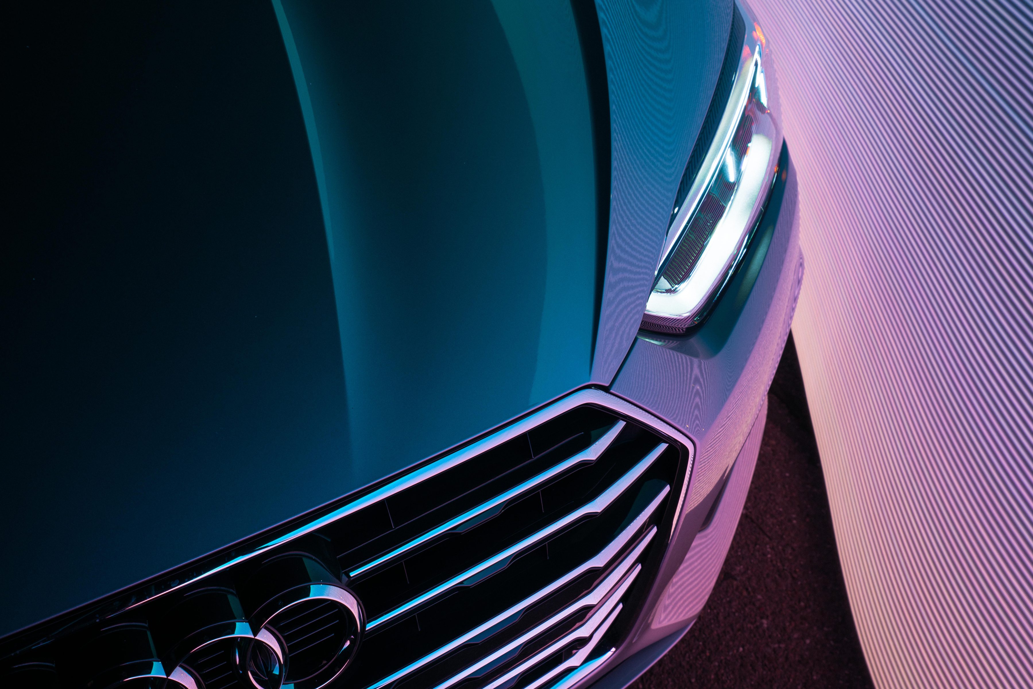 Close-up of a car’s front grille and headlight, illuminated by blue and purple lighting for a futuristic effect.