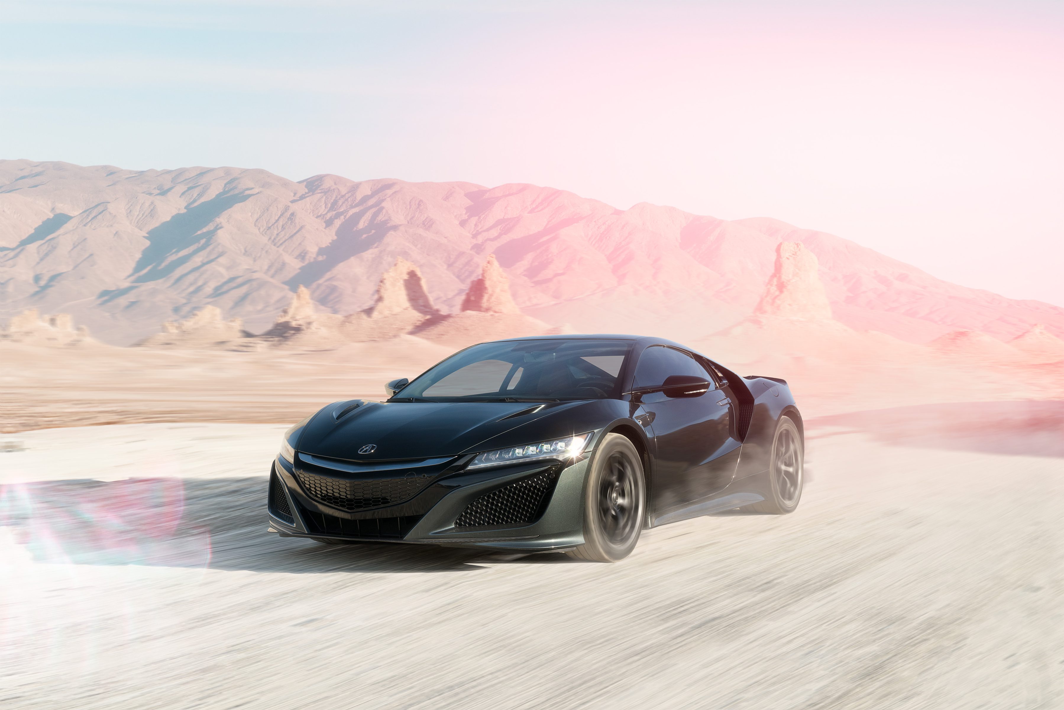 A photographer captures a black sports car driving fast on a dusty desert road, with futuristic mountains rising in the background.