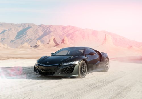 A photographer captures a black sports car driving fast on a dusty desert road, with futuristic mountains rising in the background.