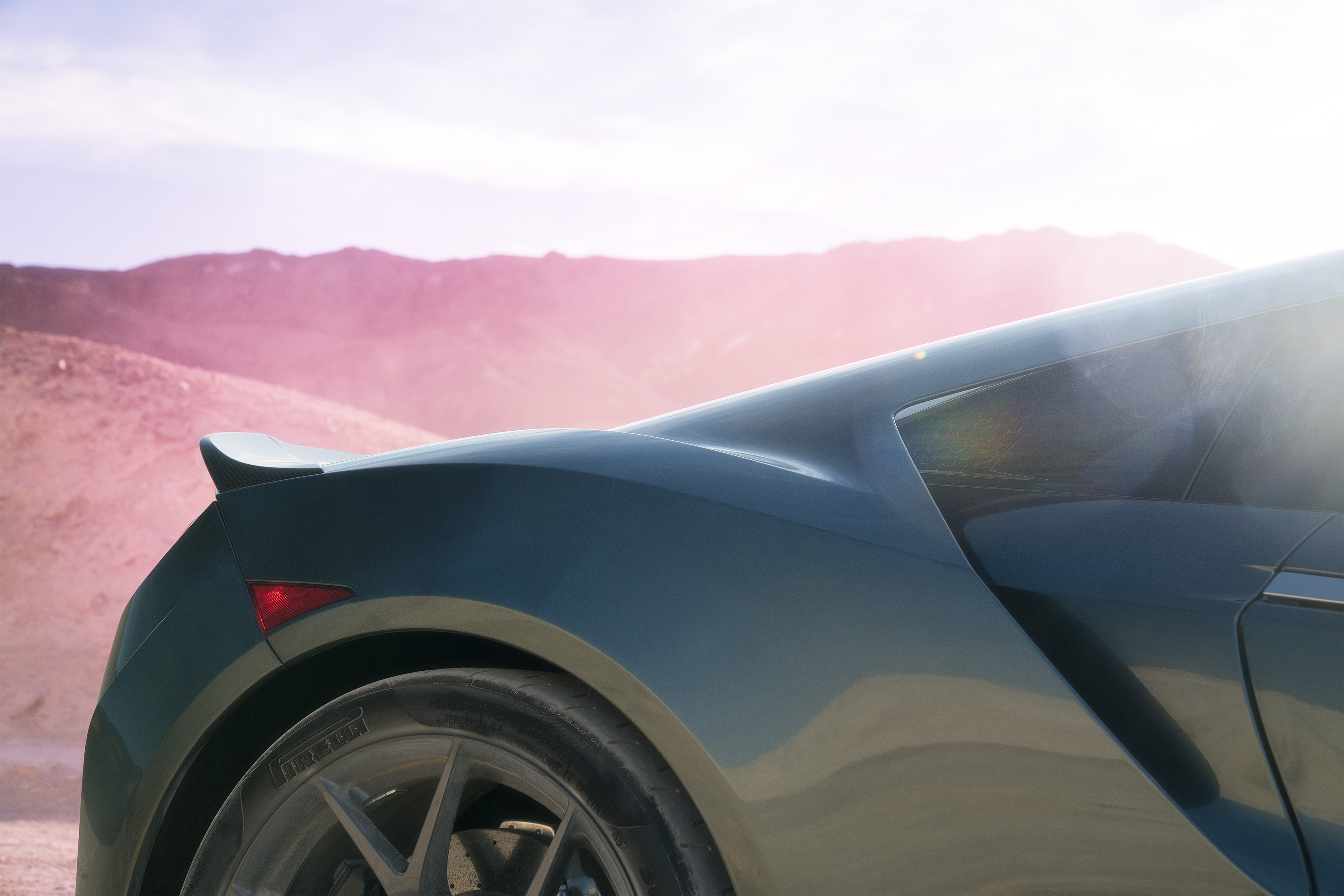 Close-up of a sports car's rear, captured by a fine artist, with mountains and pink sunlight in the background.