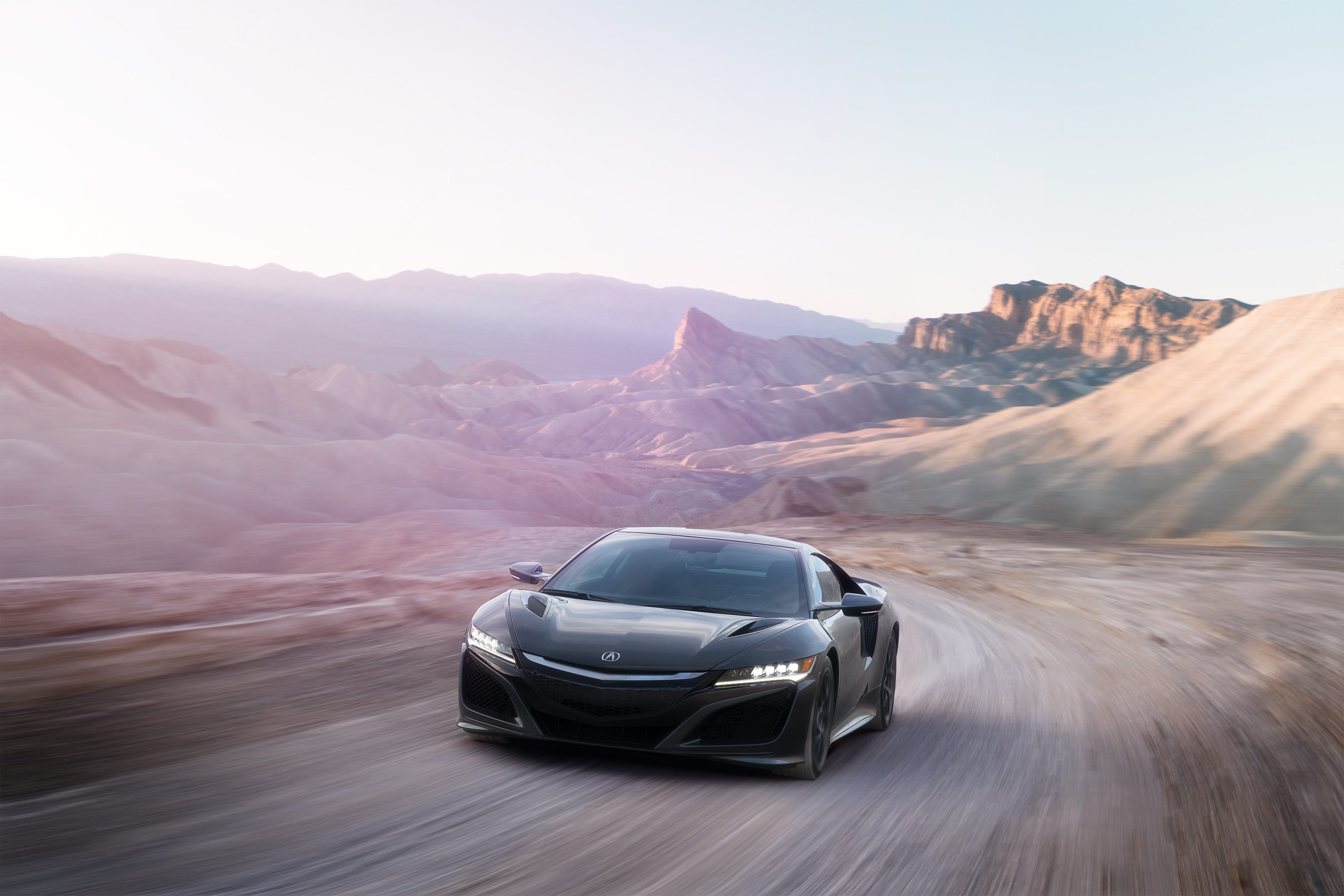A sleek black sports car driving on a winding desert road with mountains in the background at sunset, captured in the style of nighttime landscape photography.