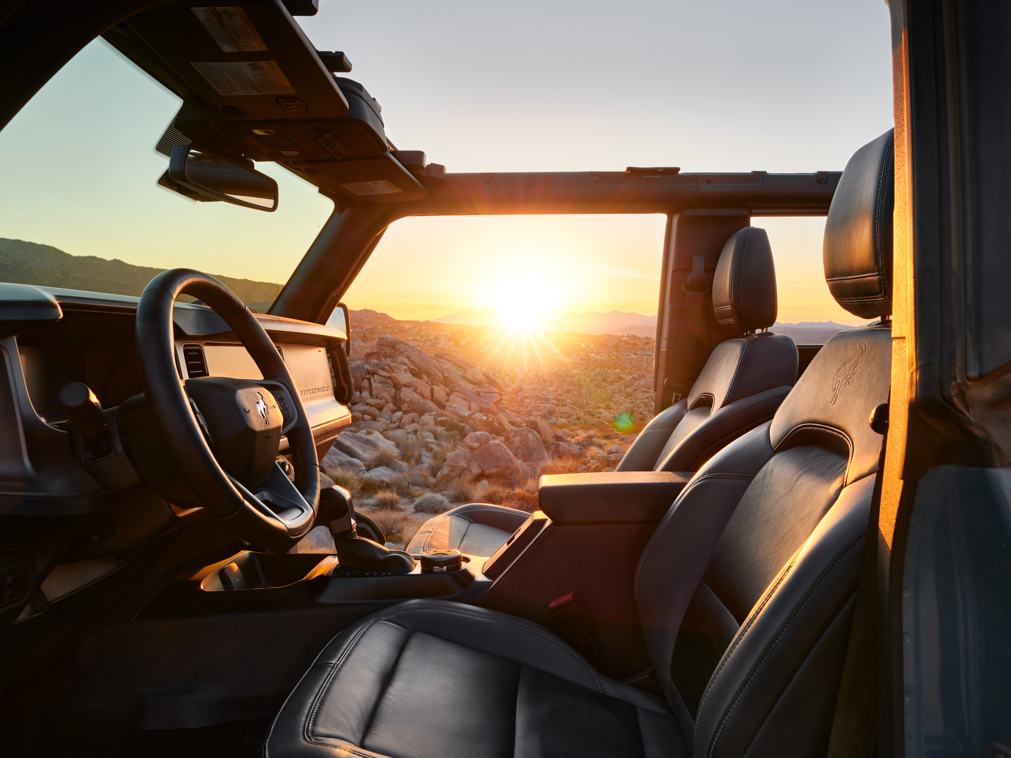 The sun sets over rocky hills, seen from inside a Jeep with the doors and roof removed, as a fine artist captures the scene through breathtaking drone light painting.