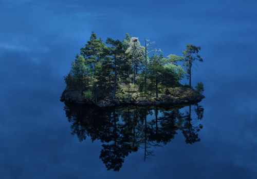 A small, tree-covered island reflected in still blue water under a clear sky, enhanced by futuristic drone light painting dancing above the tranquil scene.