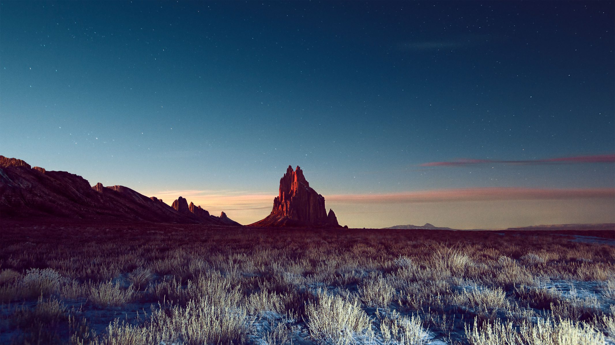 A rocky peak rises from a grassy plain under a twilight sky filled with stars, captured in stunning nighttime landscape photography by a visionary photographer.