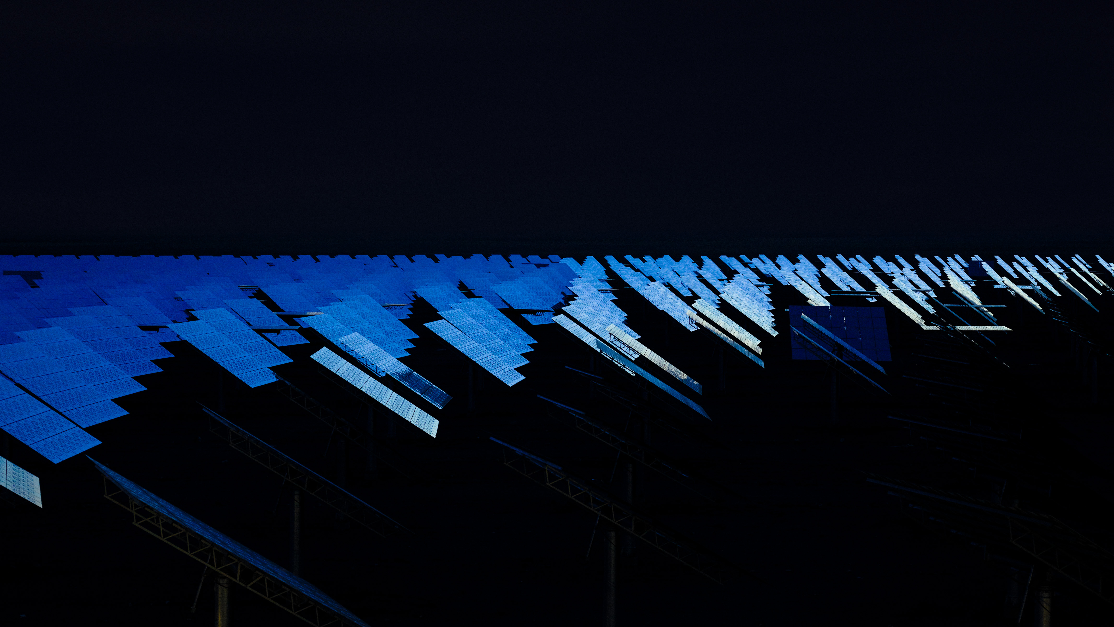 Rows of solar panels reflecting blue light, stretching into the distance against a dark background—an impressive scene of nighttime landscape photography.