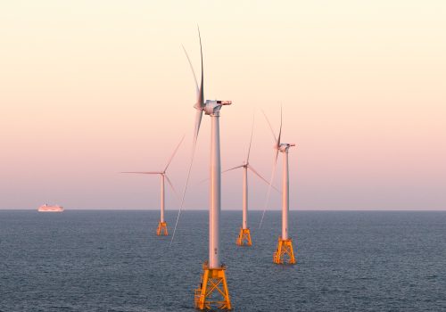 Four offshore wind turbines stand in the ocean at sunset, a distant cruise ship to the left. The scene feels futuristic, as if envisioned by a fine artist capturing tomorrow’s energy landscape.