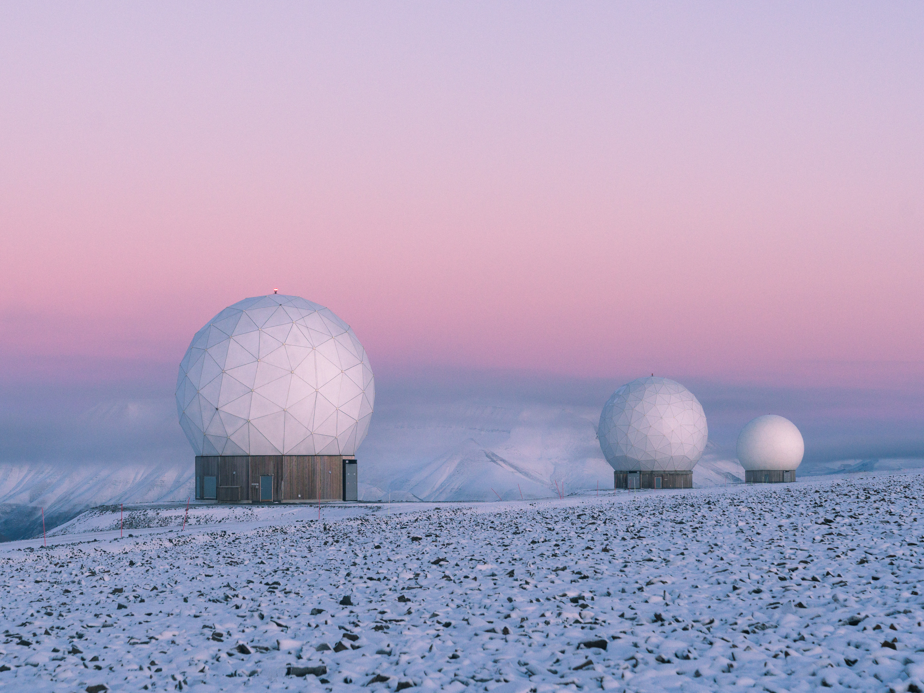 Three white geodesic domes on a snowy landscape under a pink and purple sunset sky, creating a futuristic scene perfect for any photographer.