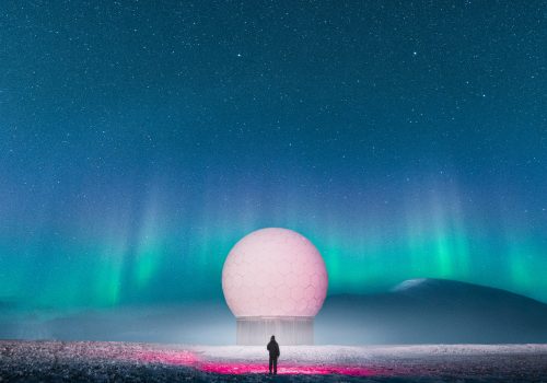 A person stands near a large white dome under an aurora-lit night sky with stars, capturing the magic of nighttime landscape photography.