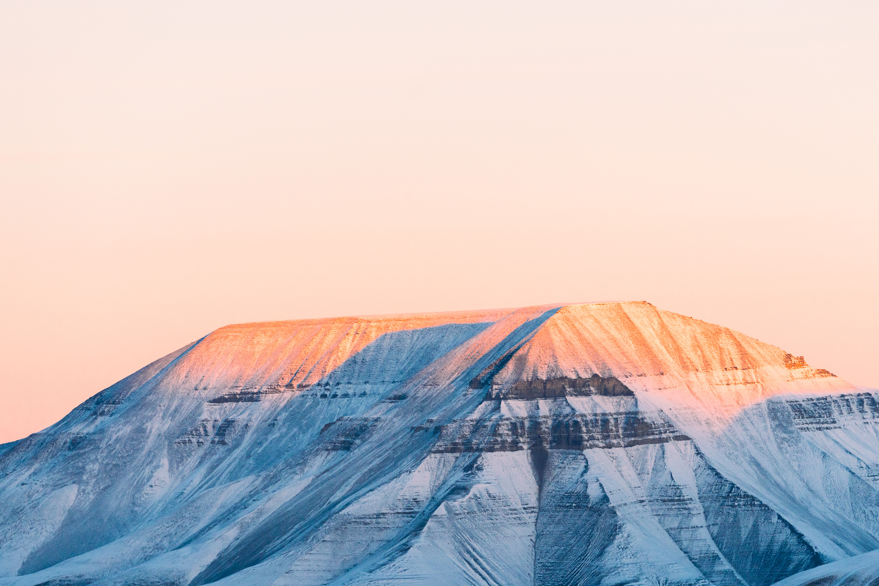 Snowy flat-topped mountain bathed in warm sunrise light, with futuristic drone light painting illuminating the pale pink sky.