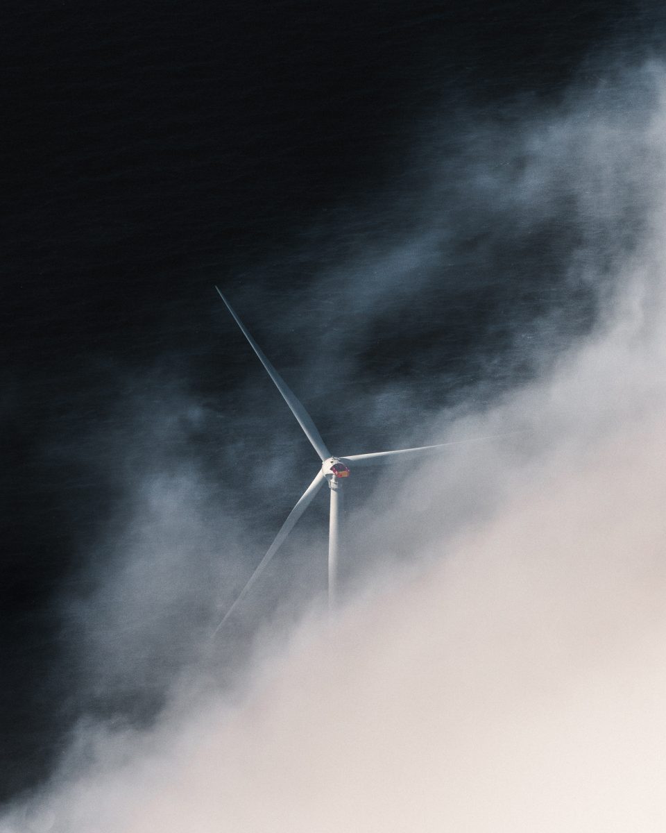 A wind turbine emerges through thick fog, with dark water visible in the background—a scene reminiscent of futuristic nighttime landscape photography.