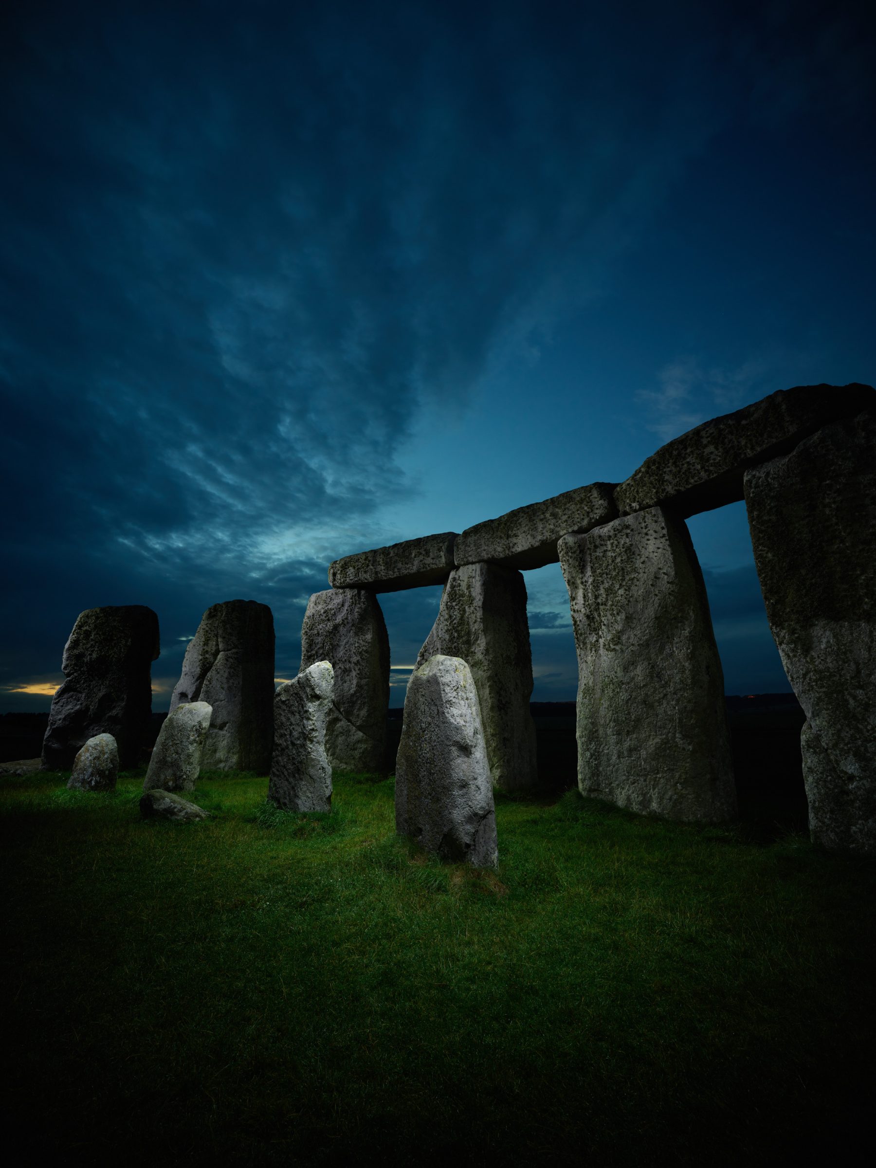 Stonehenge standing stones at dusk under a dramatic, cloudy blue sky, illuminated by mesmerizing drone light painting.