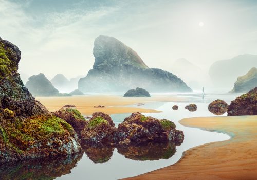 Rocky, moss-covered beach with tide pools, misty sea stacks, and a lone figure in the distance beneath a hazy sky—subtle traces of drone light painting linger in the air, adding an ethereal touch to this fine artist’s coastal scene.