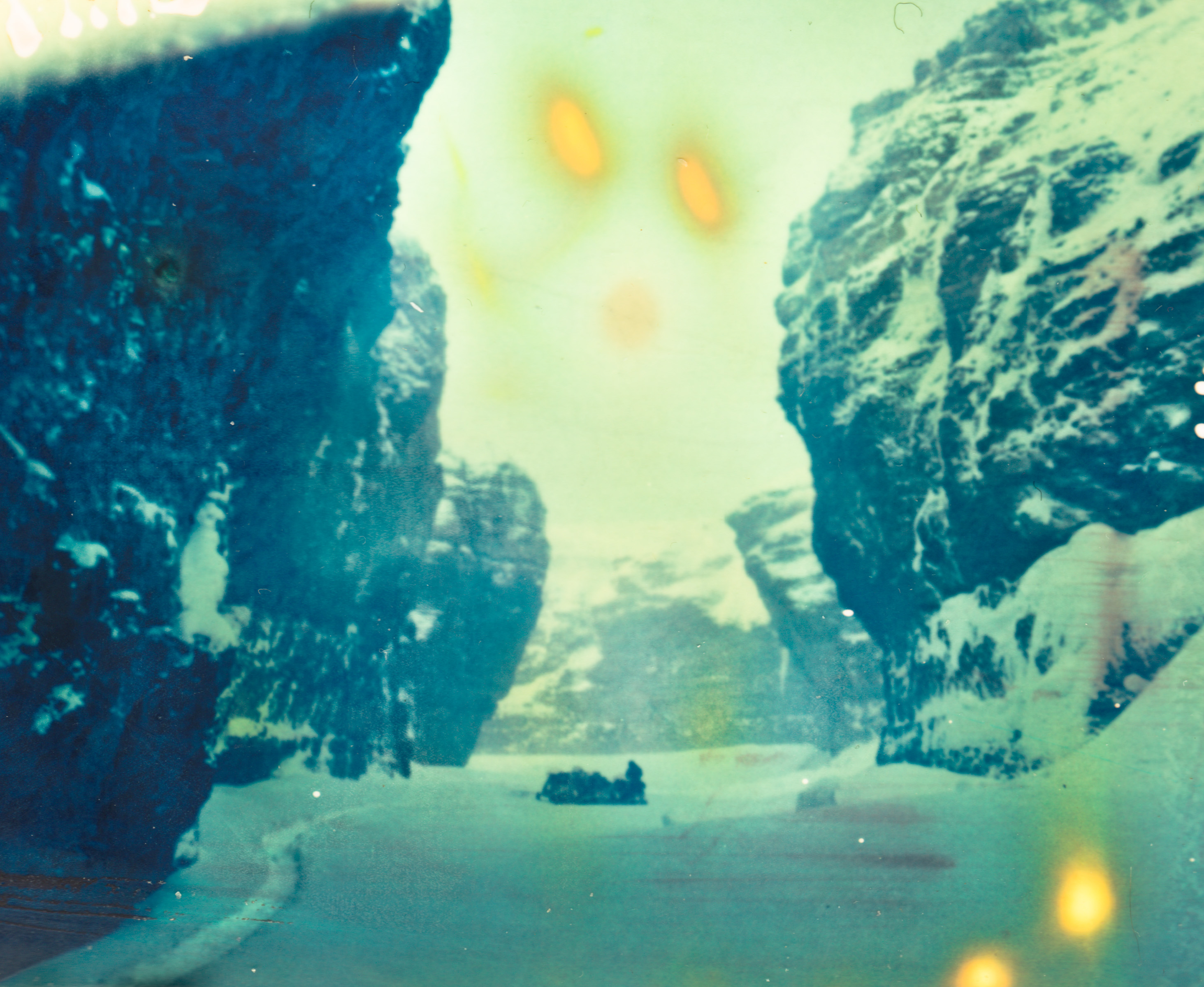 A small boat moves through a snowy canyon flanked by towering, rugged cliffs under a pale sky, capturing a scene worthy of a fine artist or photographer’s eye.