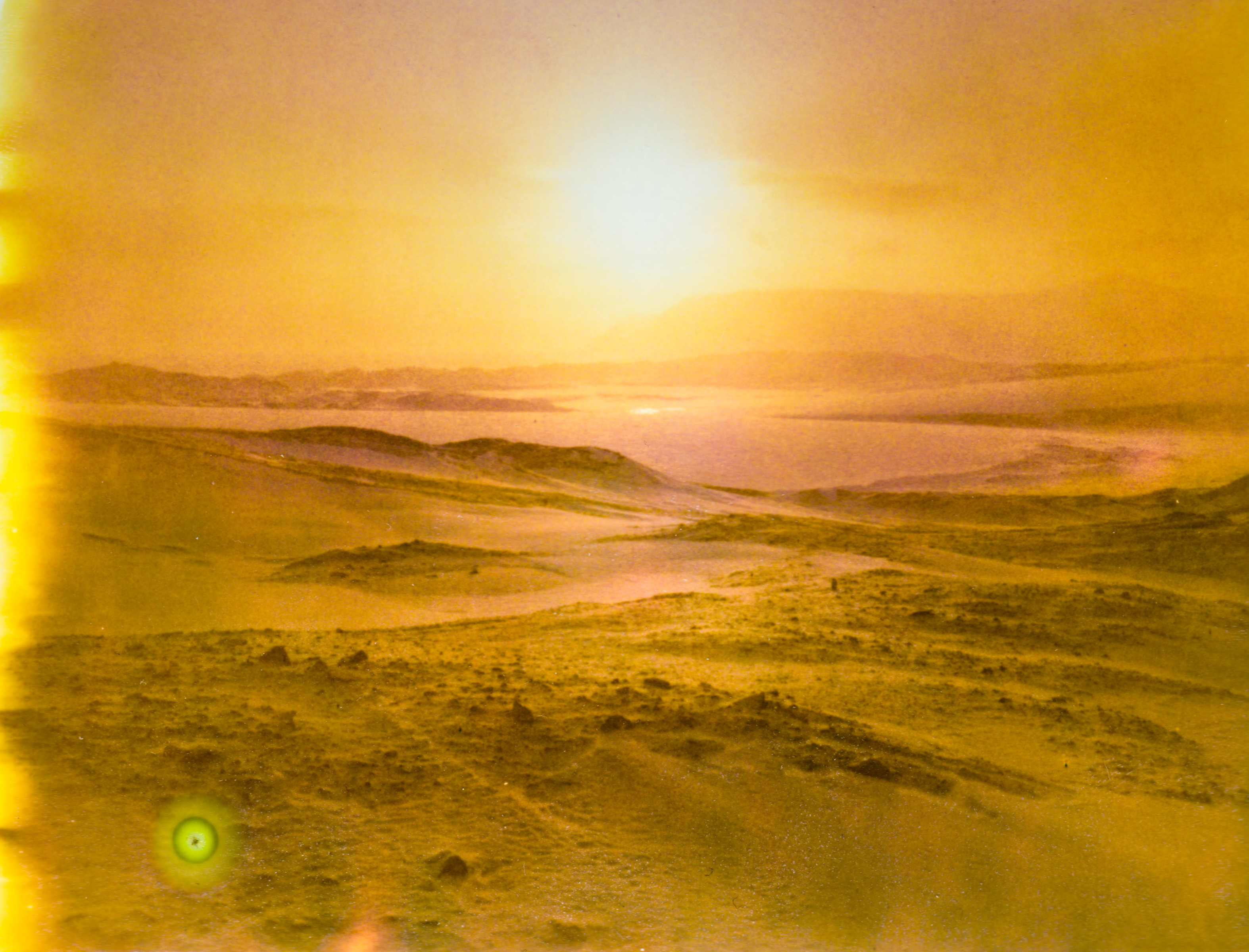 Hazy yellow landscape with rolling hills and a glowing sun low on the horizon, casting bright light—reminiscent of a fine artist’s palette or an ethereal drone light painting.