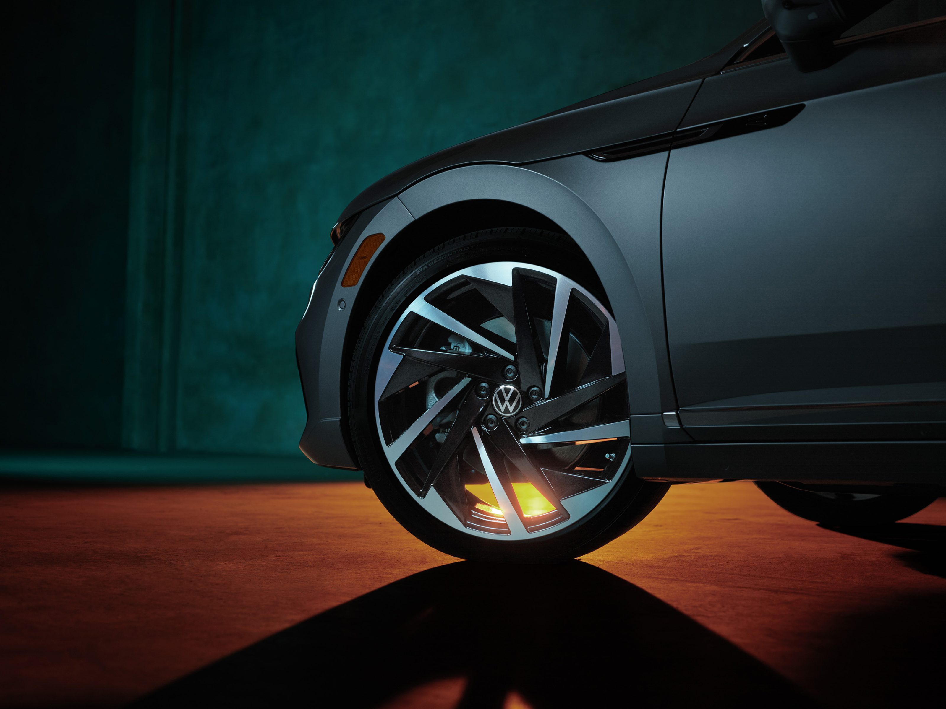 Close-up of a Volkswagen car’s front wheel with dramatic lighting and glowing orange reflections on the floor, captured by a photographer inspired by nighttime landscape photography.