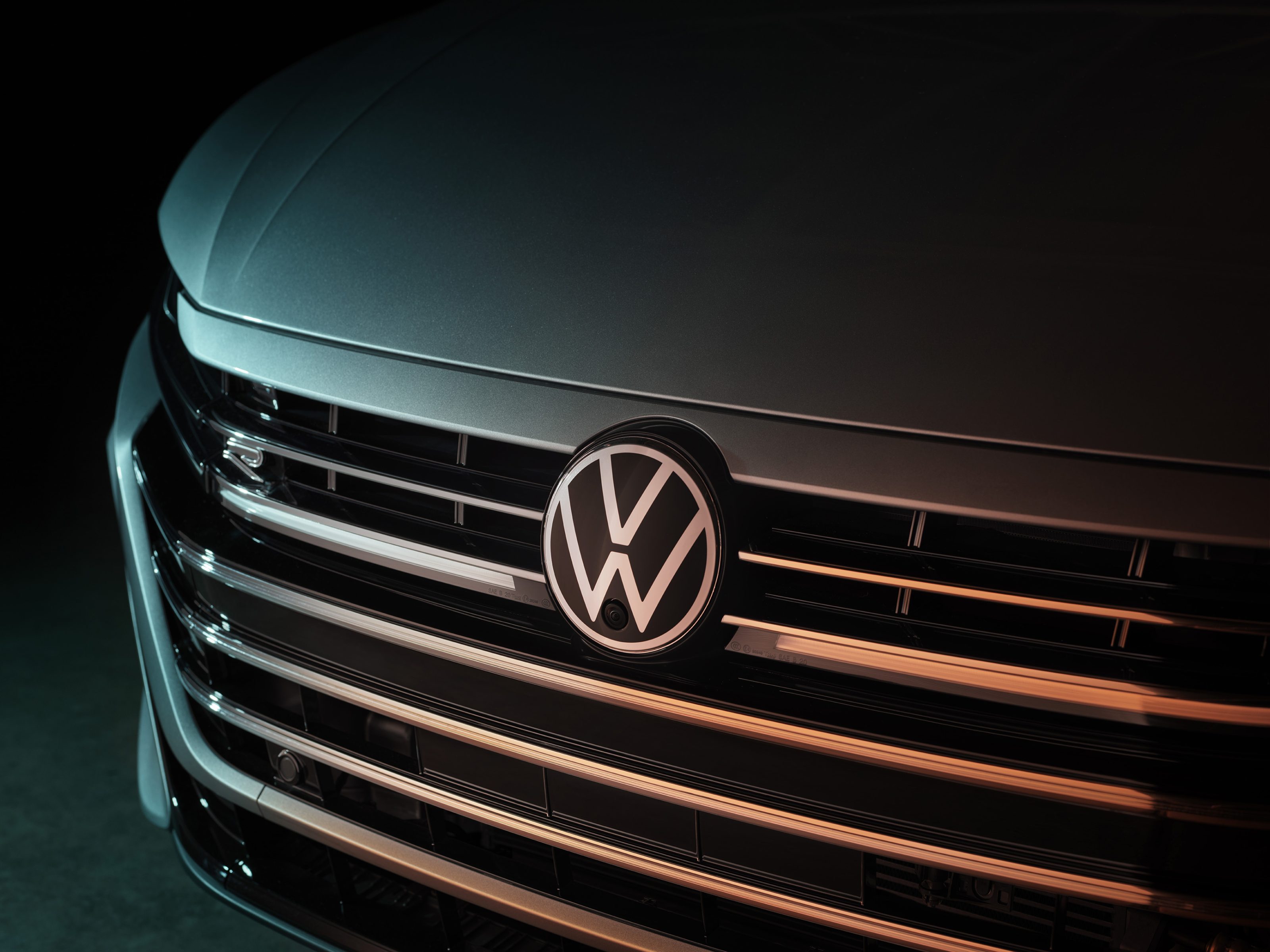 Close-up of a Volkswagen car grille with the VW logo illuminated by soft lighting, capturing the detail with the precision of a fine artist and the dramatic flair found in nighttime landscape photography.