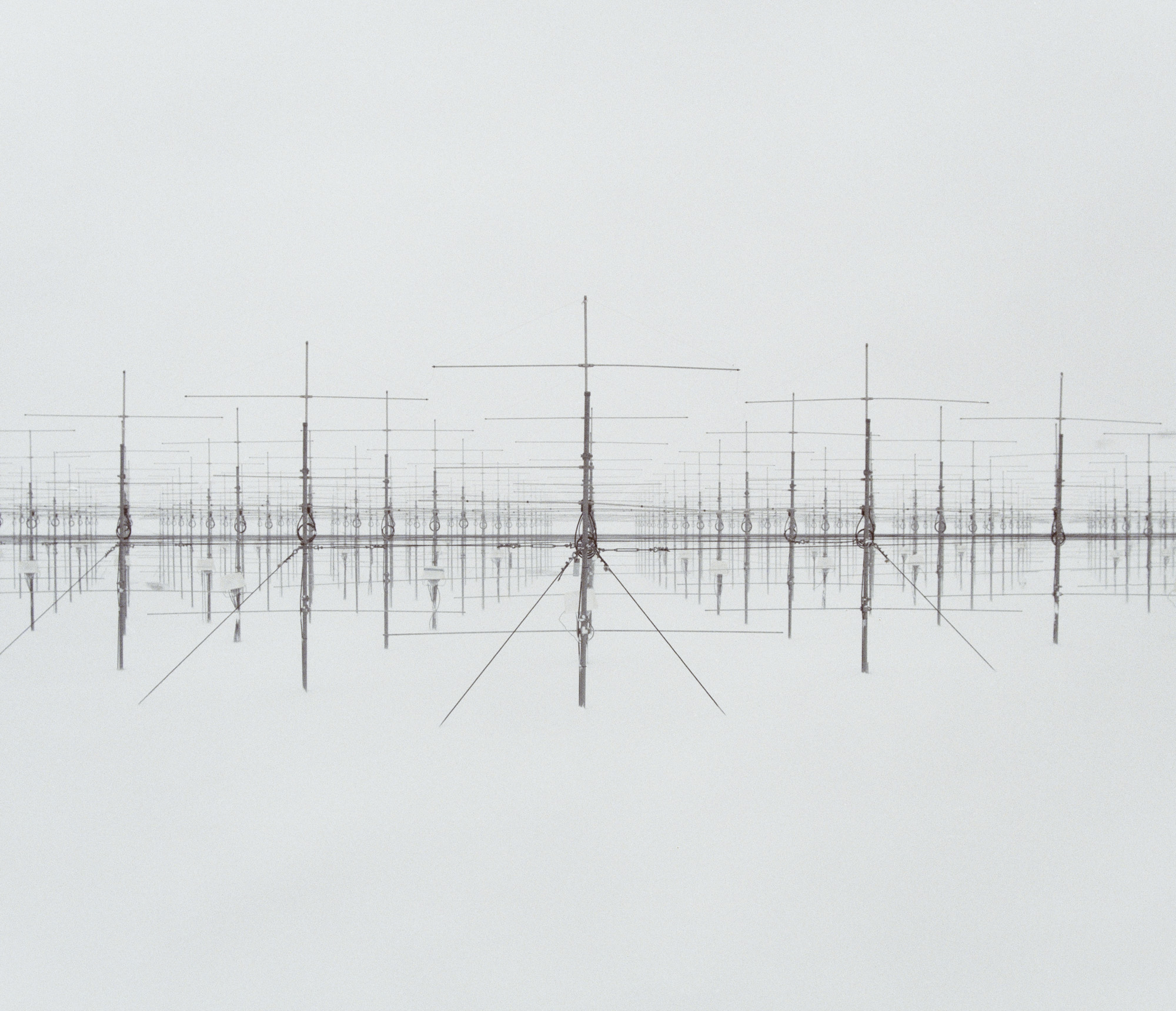 Rows of tall, metal antenna structures are reflected on a smooth, white, and foggy surface—evoking the surreal beauty often captured in nighttime landscape photography.