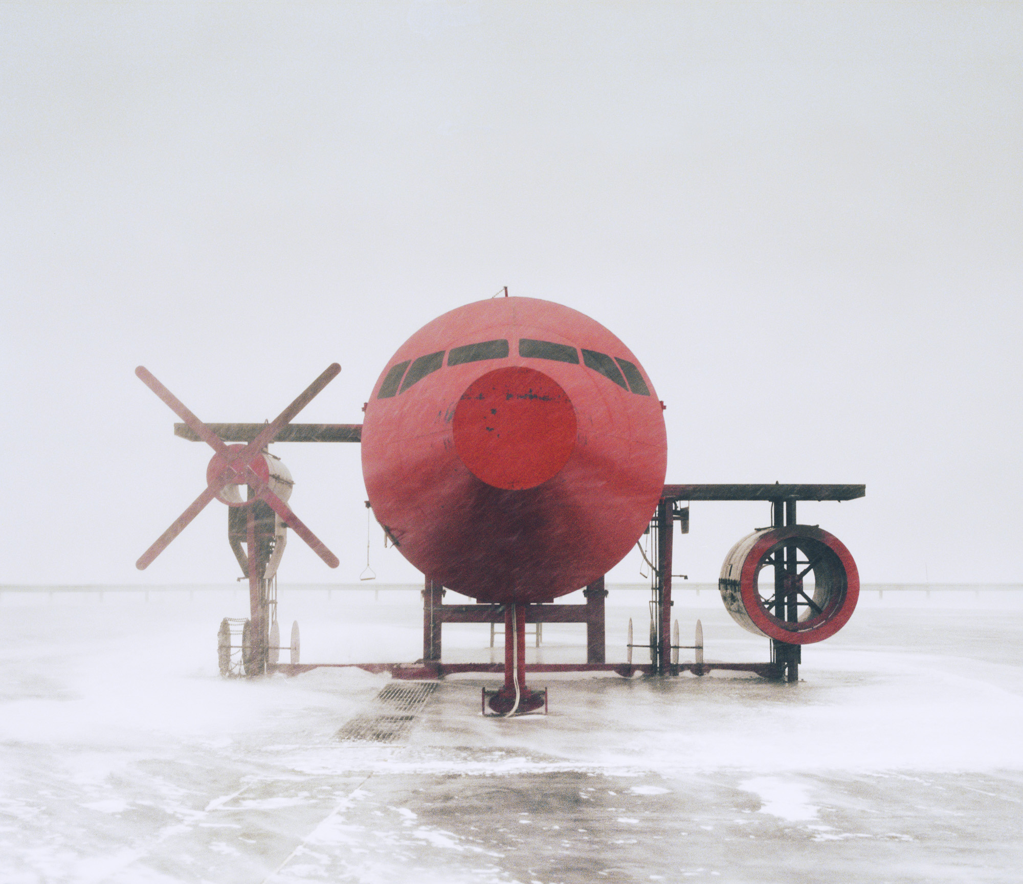 A red airplane covered in snow is parked on a snowy runway in foggy weather, its silhouette glowing with a futuristic aura reminiscent of drone light painting.