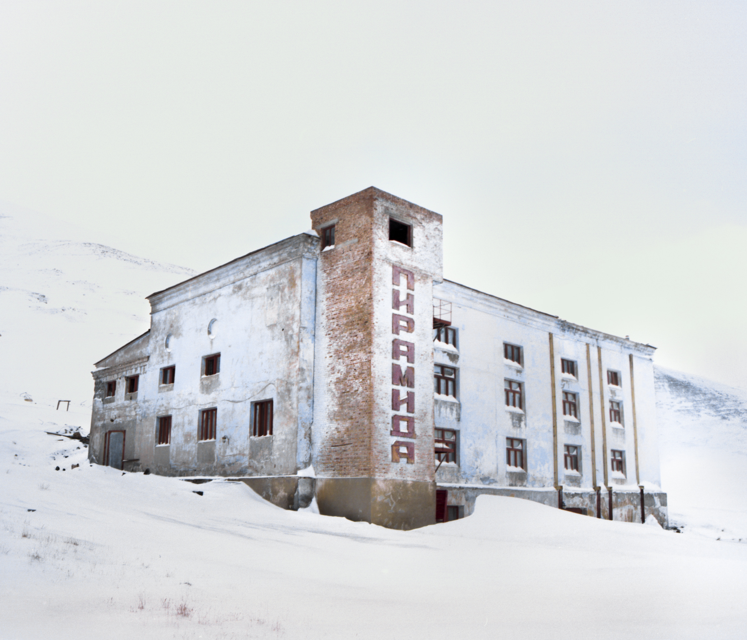 A weathered, abandoned building with Russian text stands in a snowy, desolate landscape—a haunting scene reminiscent of fine artist techniques in nighttime landscape photography.