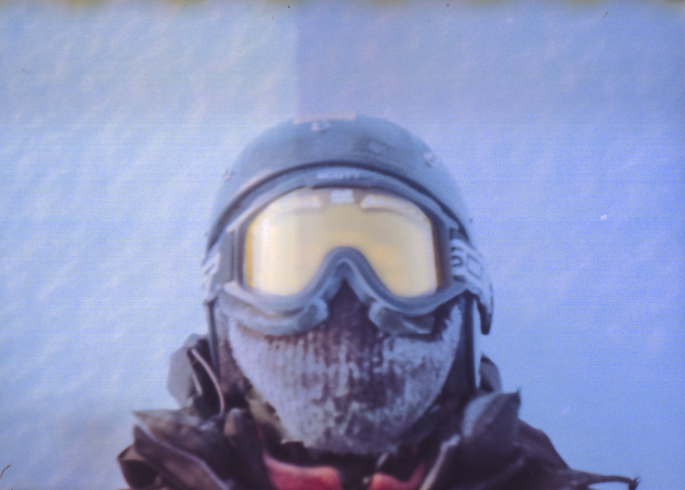 A photographer wearing ski goggles and a helmet, face covered in frost, stands in a snowy, cold environment, capturing the scene with futuristic drone light painting swirling in the wintry air.