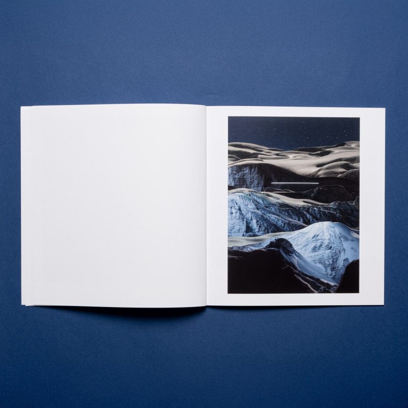 Open book on a blue surface, displaying a photo by a fine artist of a snowy, mountainous landscape beneath a starry sky.