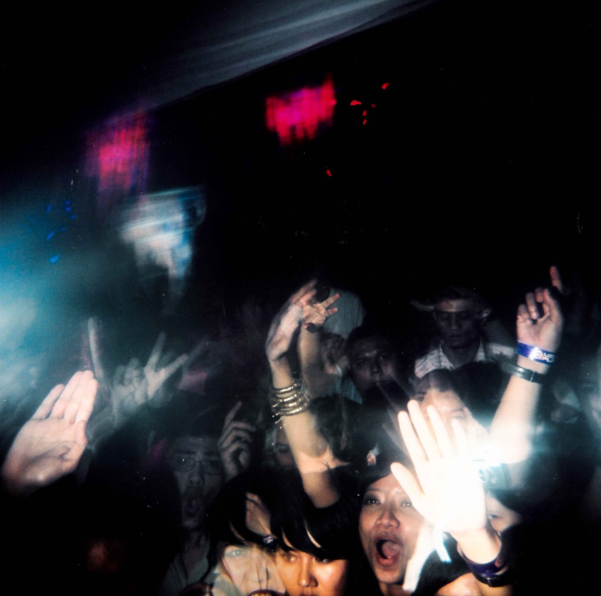 A crowd of people with raised hands enjoys a dark, energetic concert as futuristic drone light painting illuminates the scene.