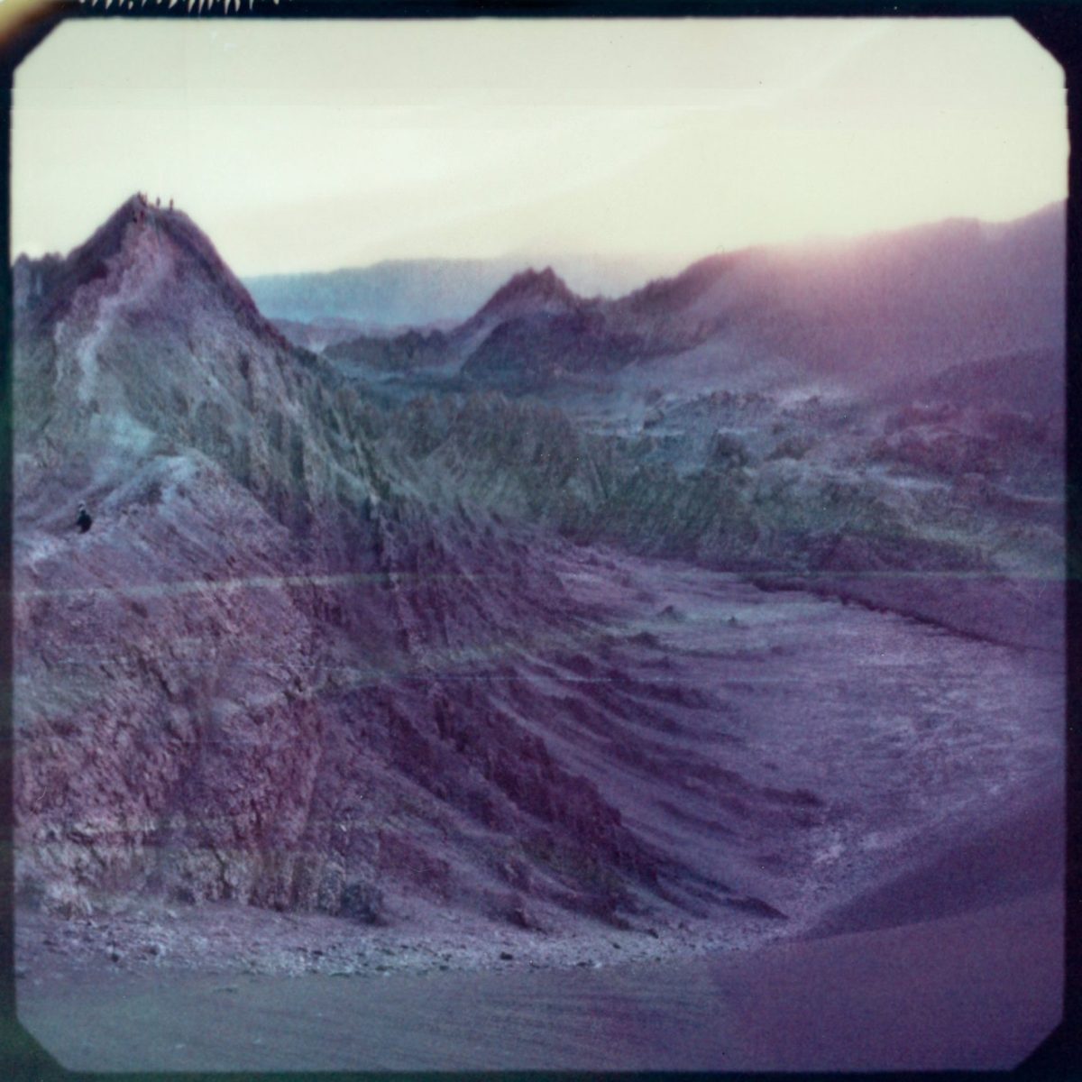 Purple-hued mountains and ridges at sunset, with a few small figures visible on the peak—perfect for a photographer capturing stunning nighttime landscape photography.