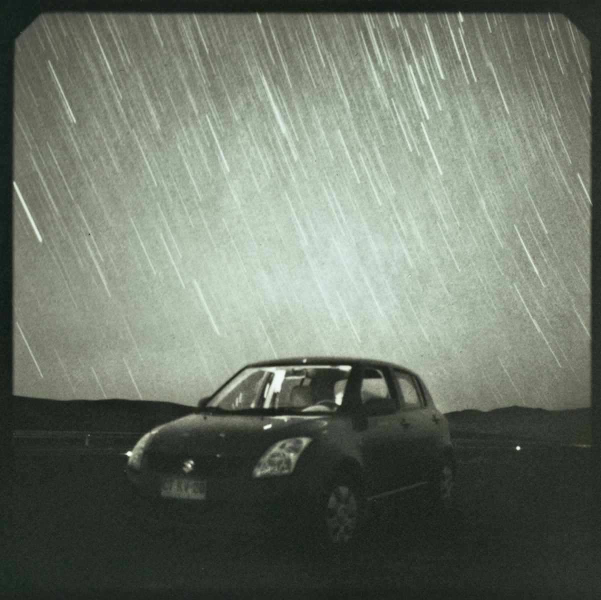 A car parked under a night sky with long star trails, captured using a long exposure, creates a stunning example of nighttime landscape photography.