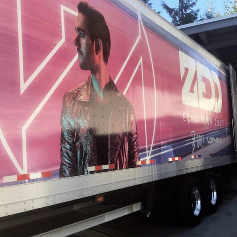 Truck with a large Zedd Echo Tour 2017 poster featuring Zedd in a shiny jacket on the side, set against striking nighttime landscape photography.