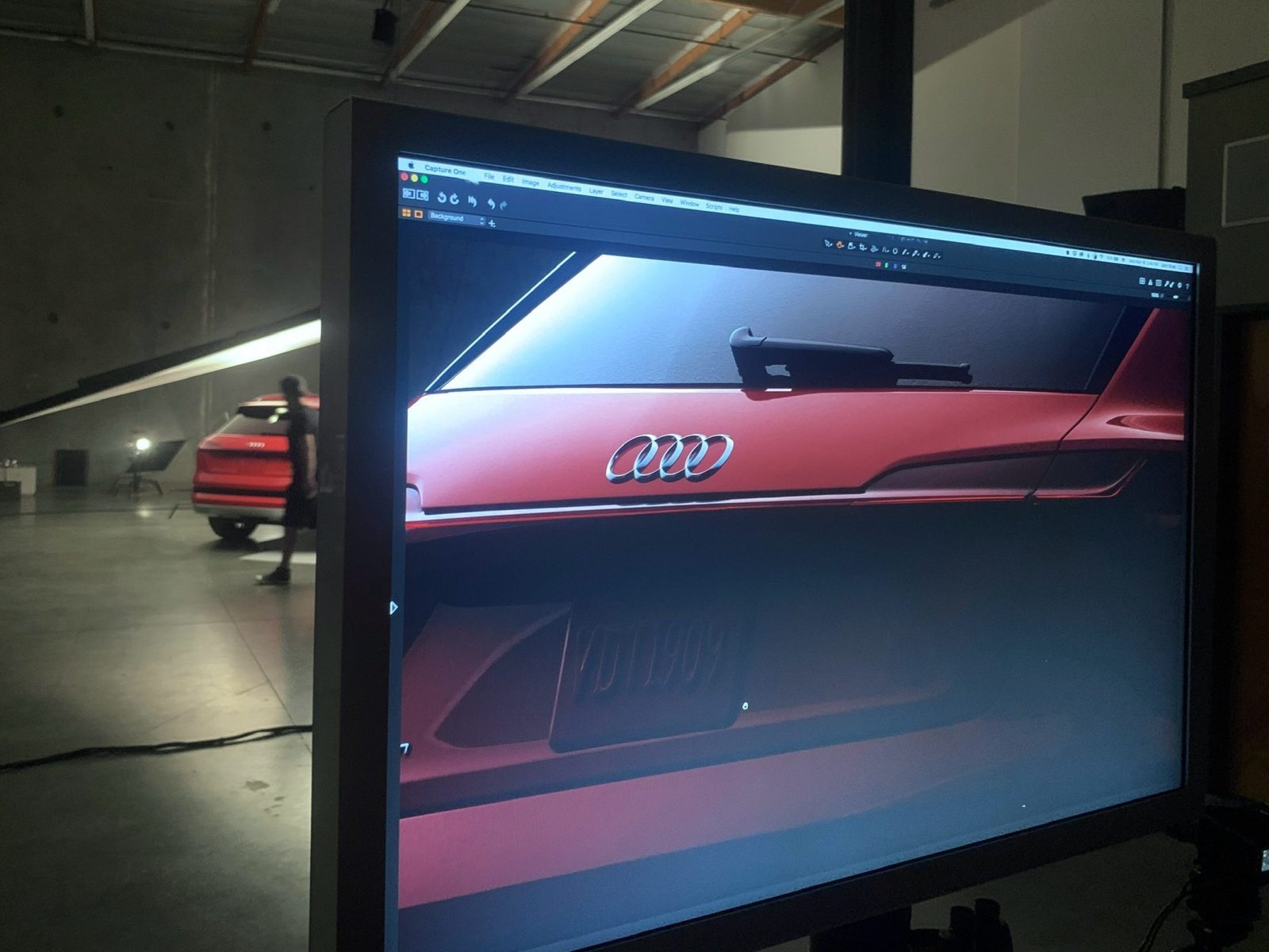 A computer screen shows a close-up photo of a red Audi SUV in a photography studio, captured by a skilled photographer.