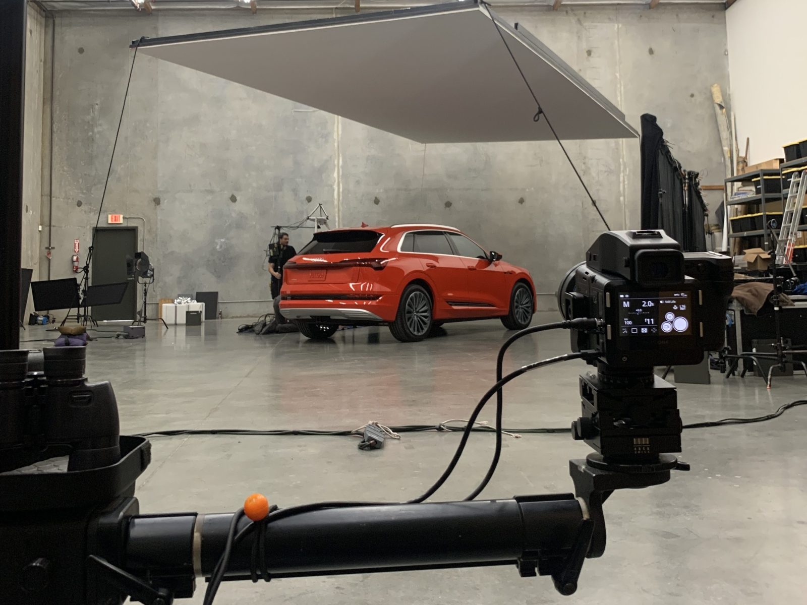 A red SUV is photographed in a studio with futuristic lighting equipment, camera gear, and hints of drone light art visible.