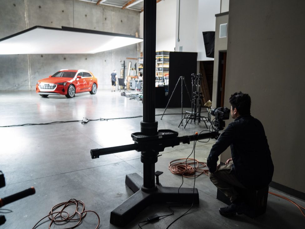 A photographer prepares to shoot a red car in a spacious, professional studio with lighting equipment, inspired by the creative techniques of nighttime landscape photography.